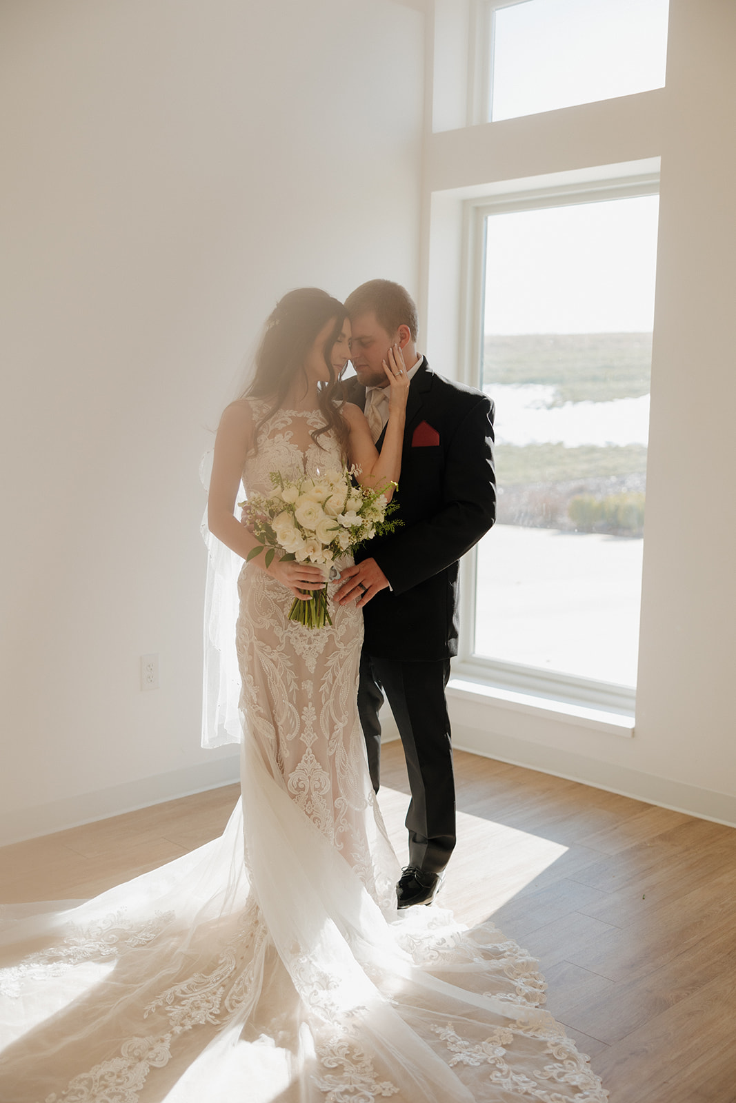 Bride and groom stand forehead to forehead by the window, her bouquet in hand and sunlight glowing around them—pure wedding day magic by a madison wedding photographer.