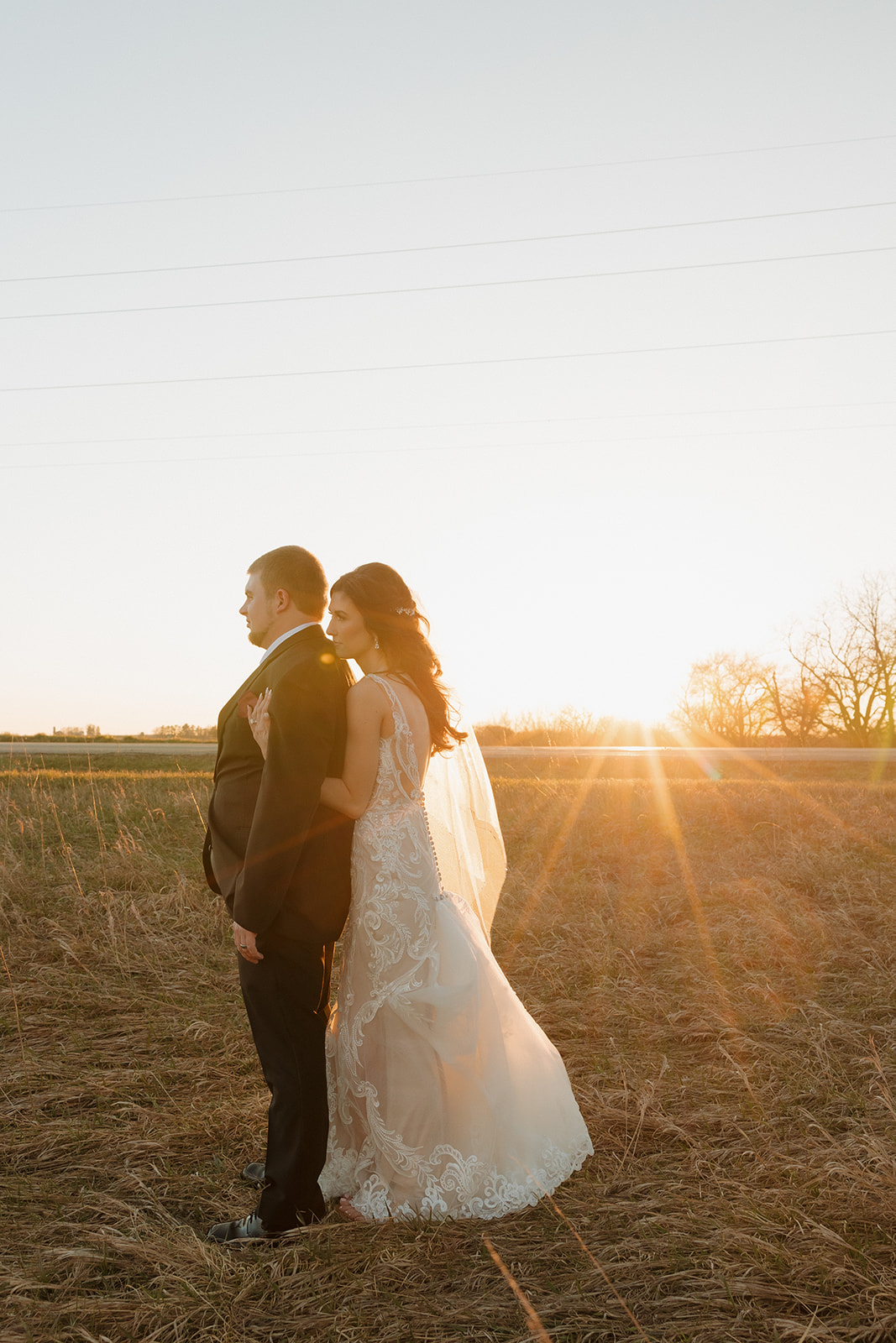 Bride hugs groom from behind as they stand in a quiet field at sunset—this madison wedding photographer moment is all romance and light flare.