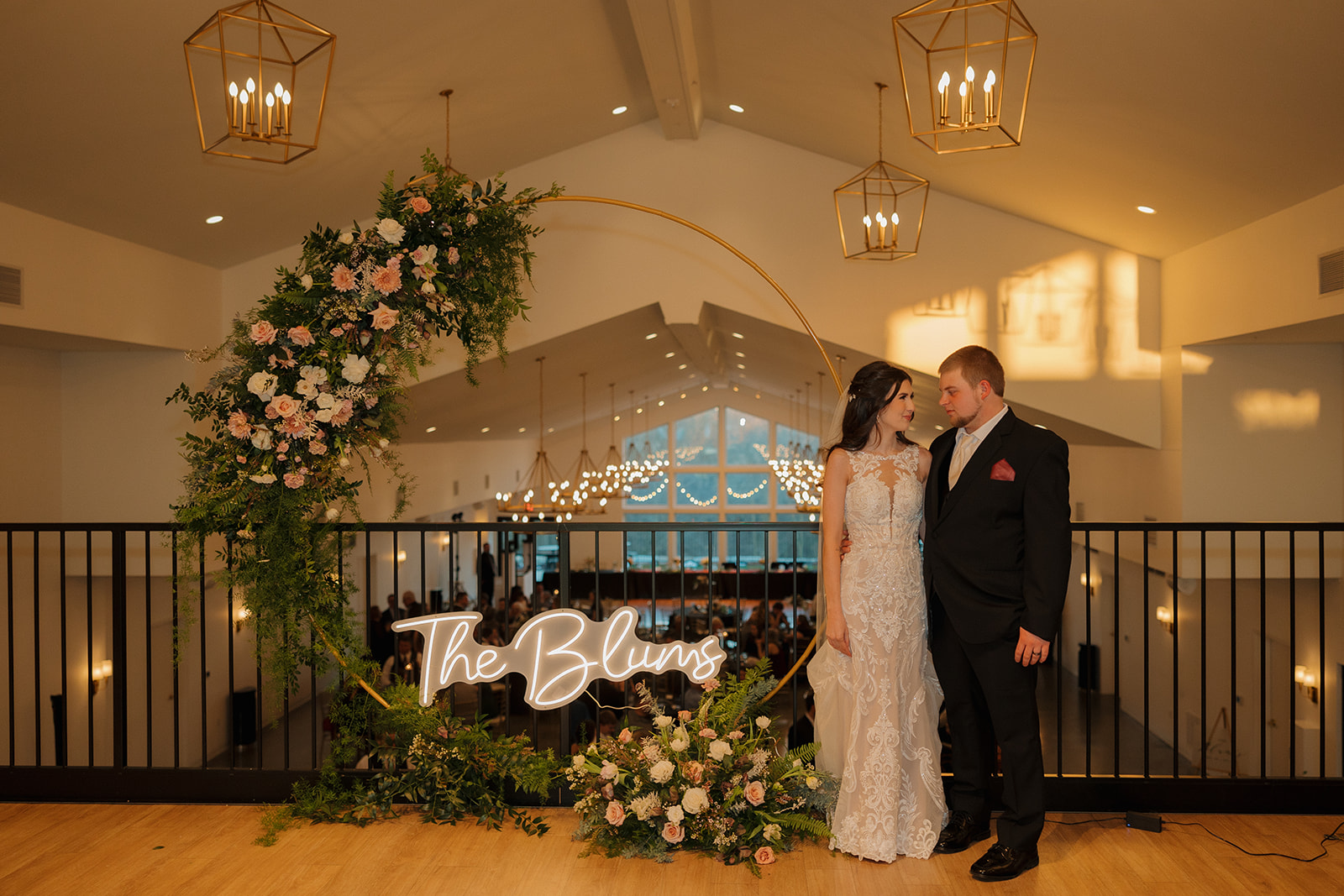 Bride and groom stand beneath a circular floral arch with their last name glowing in neon—modern elegance meets warm evening light, captured by a madison wedding photographer.