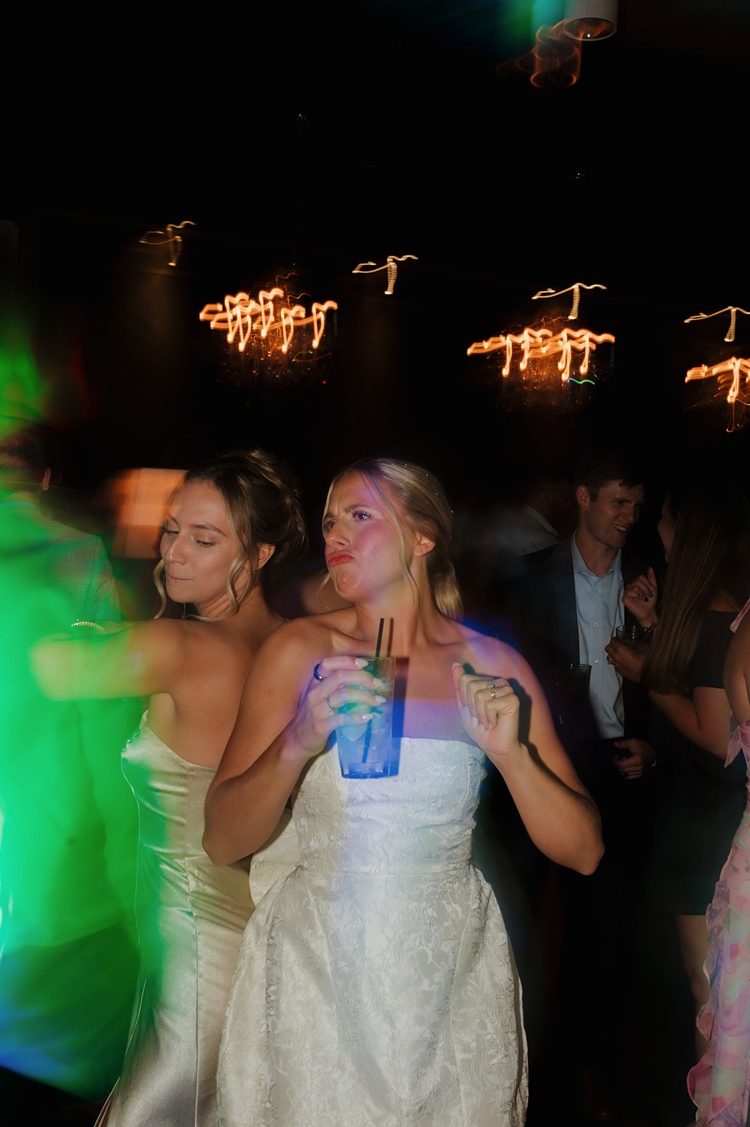 Bride dancing with a bridesmaid, drink in hand, under moody club lights during a wedding in Wisconsin.