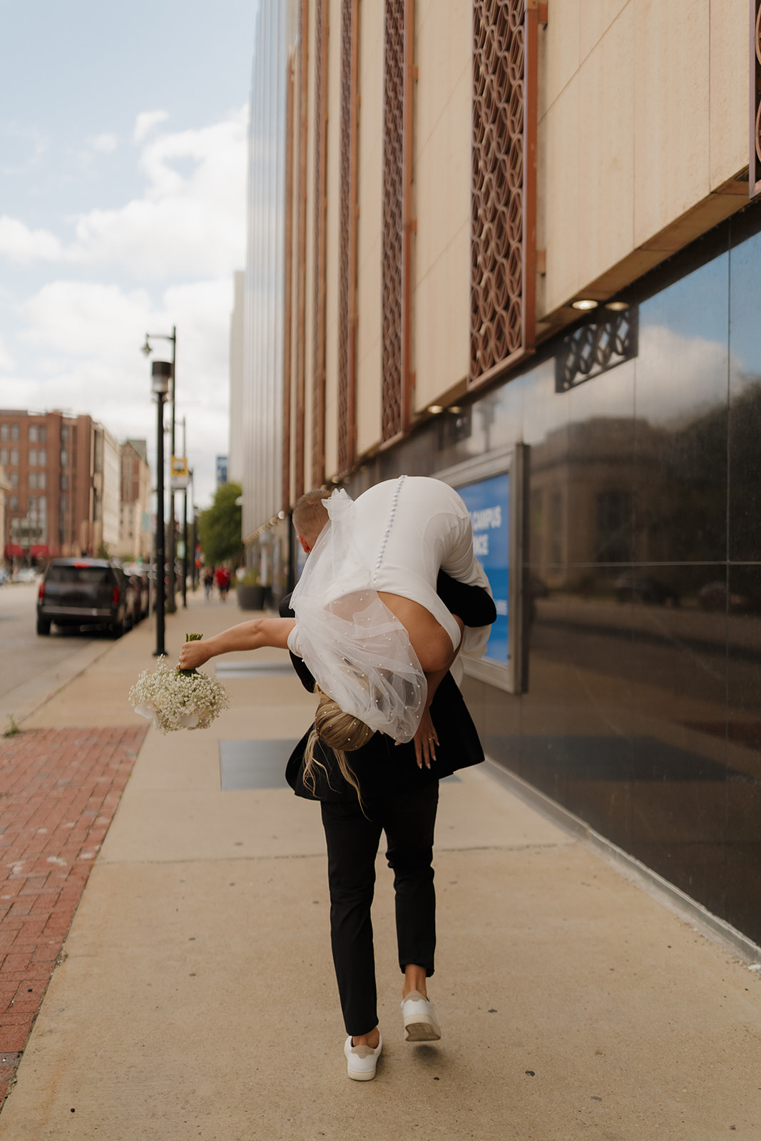 Groom lifts bride over his shoulder in a silly celebration to carry her back to their hotel after wedding in Wisconsin.