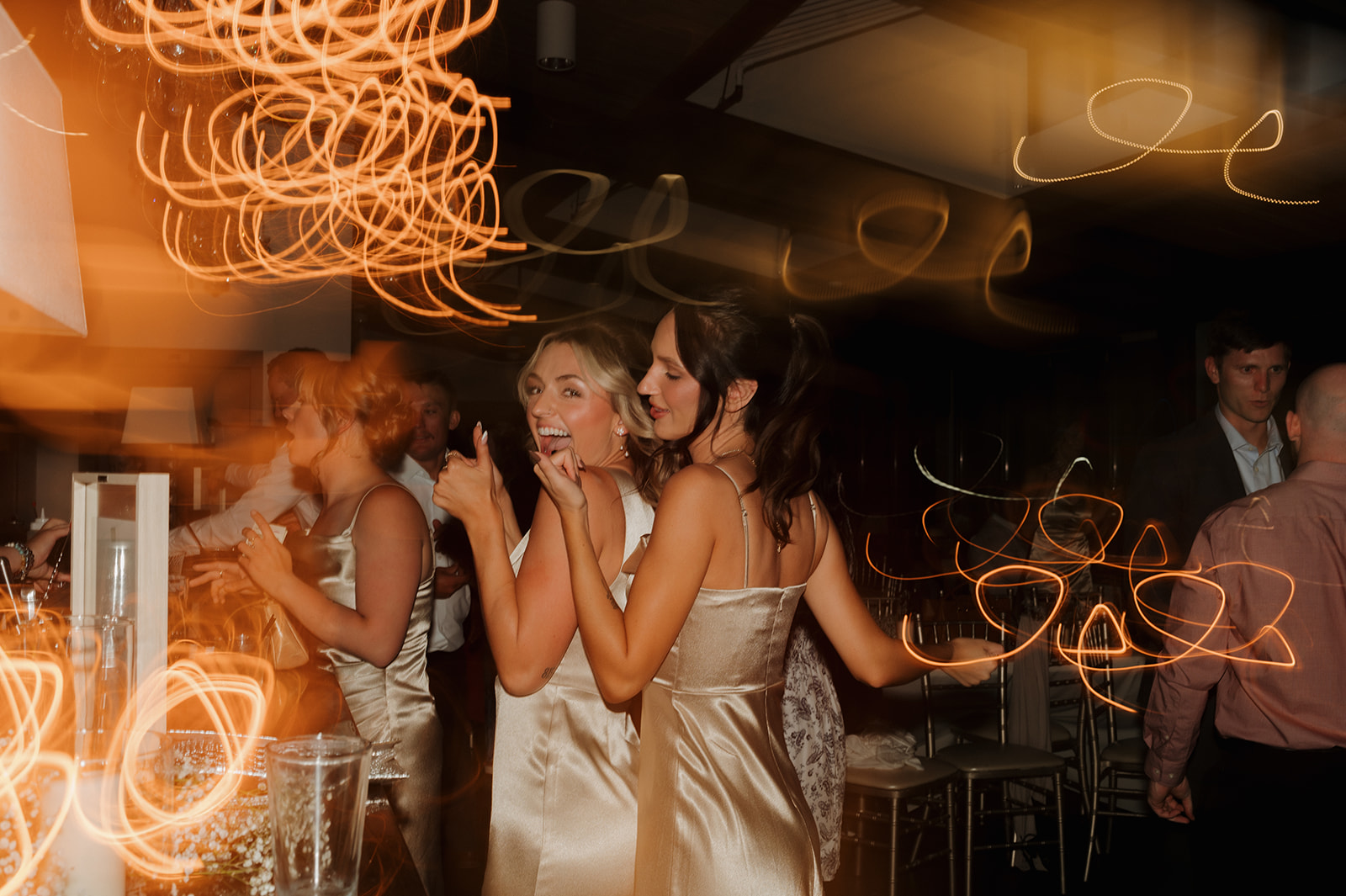 Bridesmaids dancing at the bar under golden lights, caught in a fun, blurry motion shot.