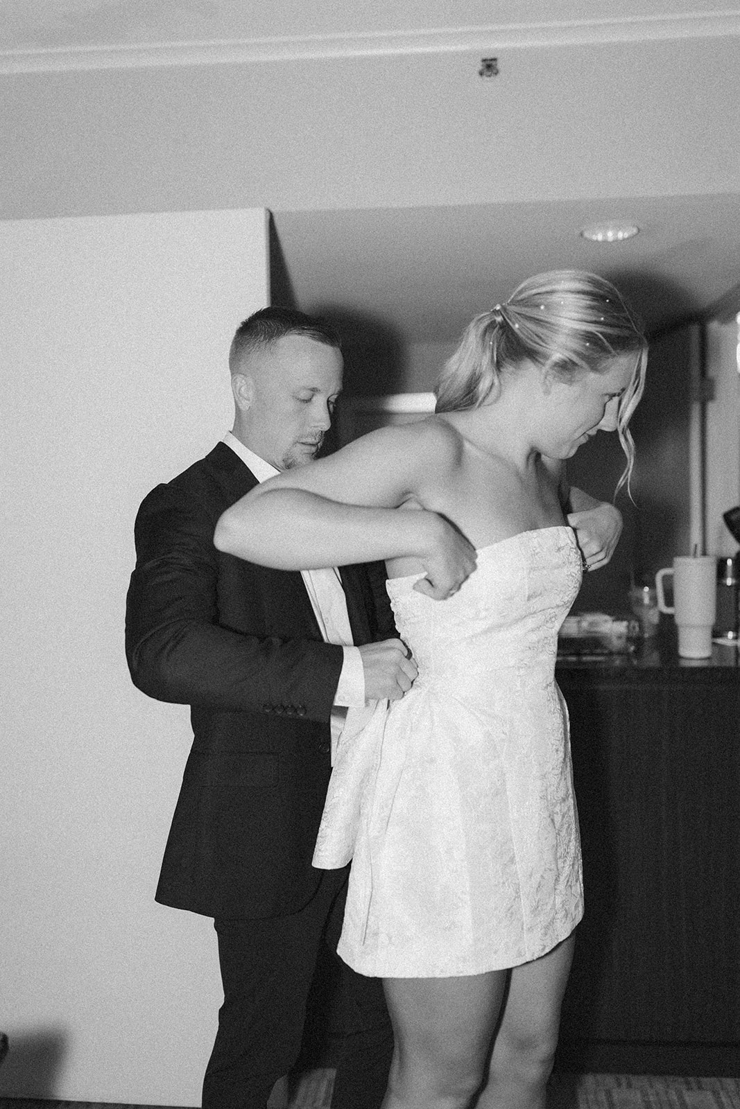 Groom helping his bride get into her reception dress, buttoning her into the mini dress.
