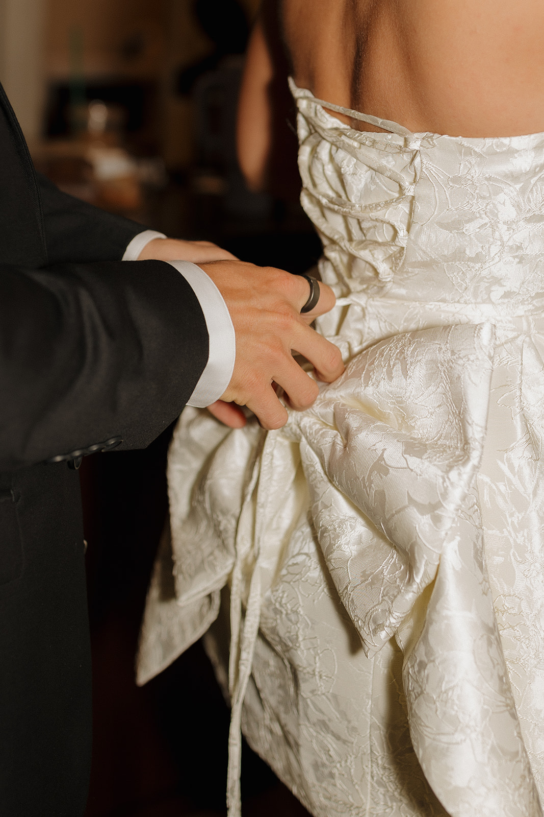 Close up of groom attaching bow to bride's reception dress.