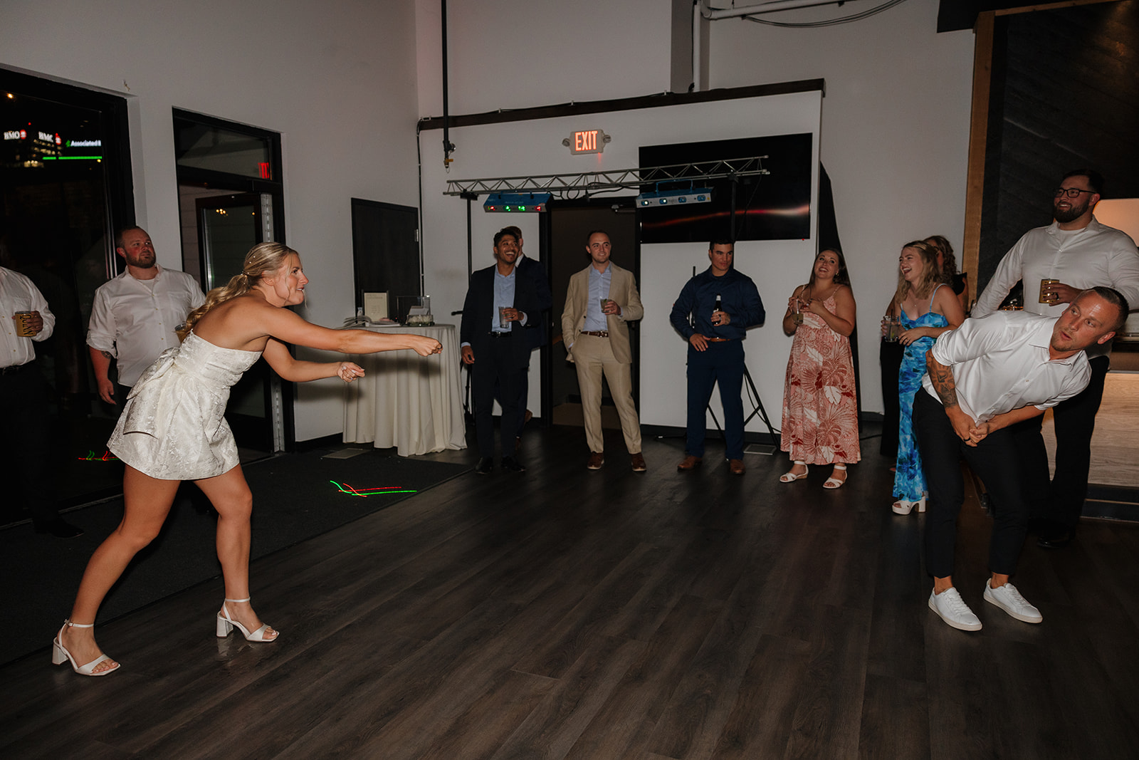 Bride and groom mid-game during a lively reception, surrounded by friends cheering them on.