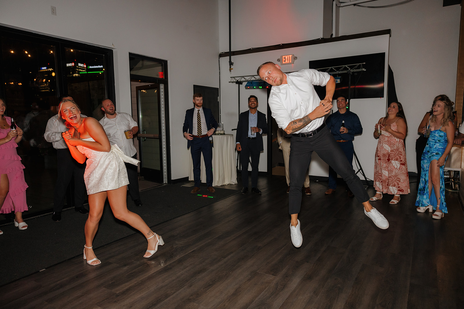 Bride laughing as the groom jumps in a dance-off moment during a playful wedding in Wisconsin.