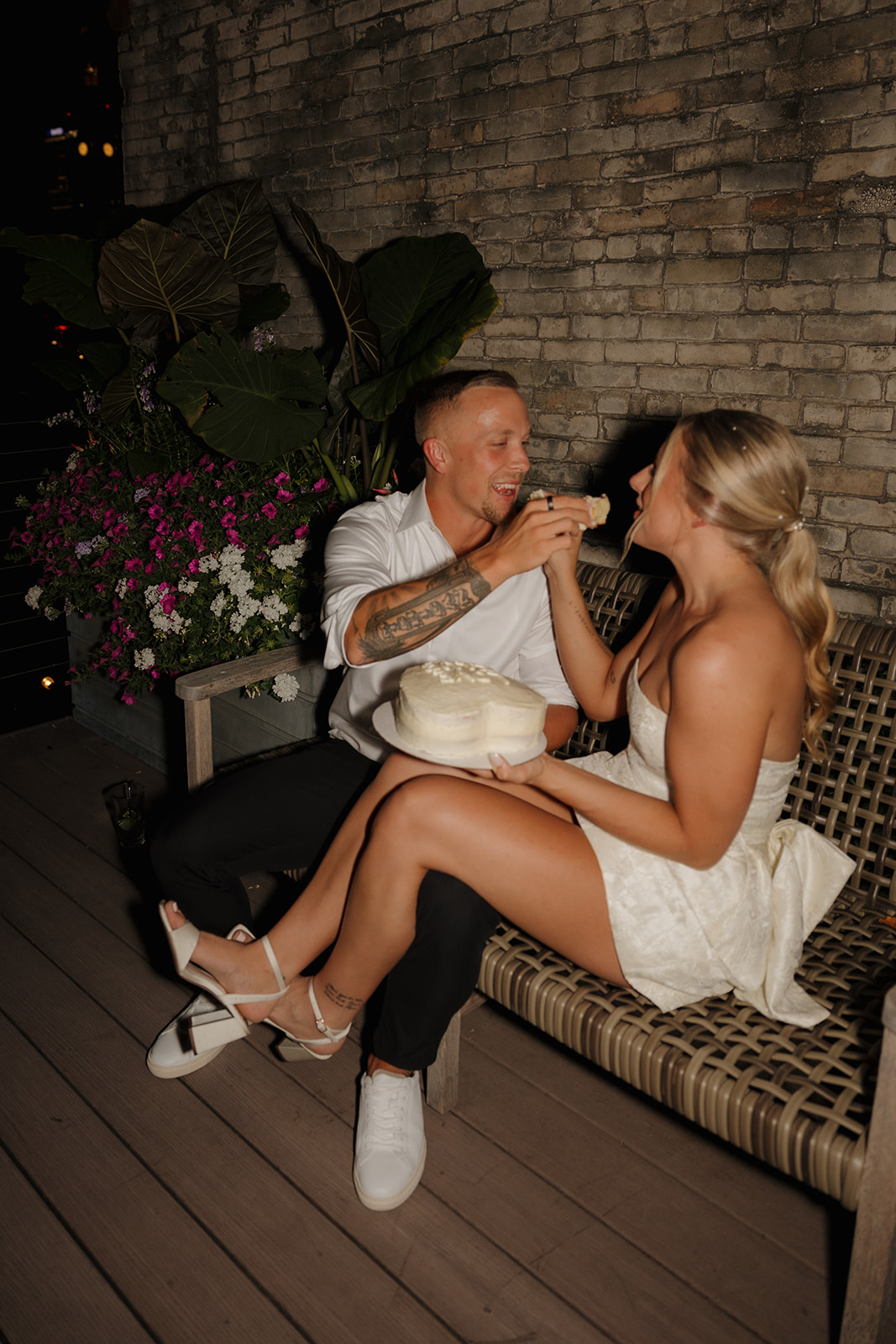 Groom feeding bride a slice of heart-shaped cake under twinkle lights at their wedding in Wisconsin.