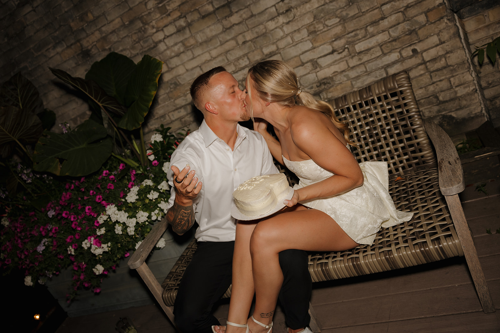Couple kissing while holding a heart-shaped cake during their reception.