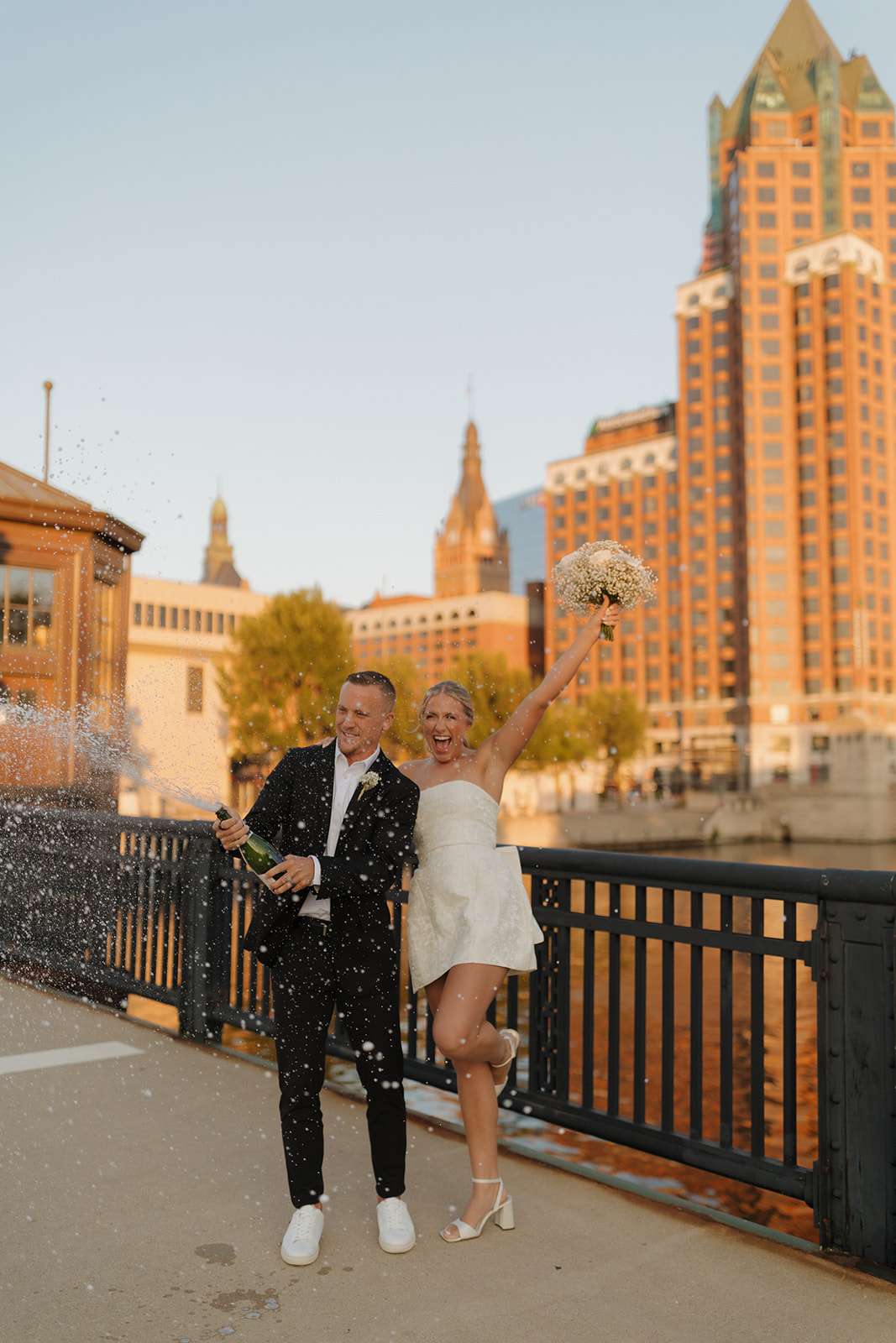 Couple popping champagne along the Milwaukee Riverwalk during their wedding in Wisconsin.