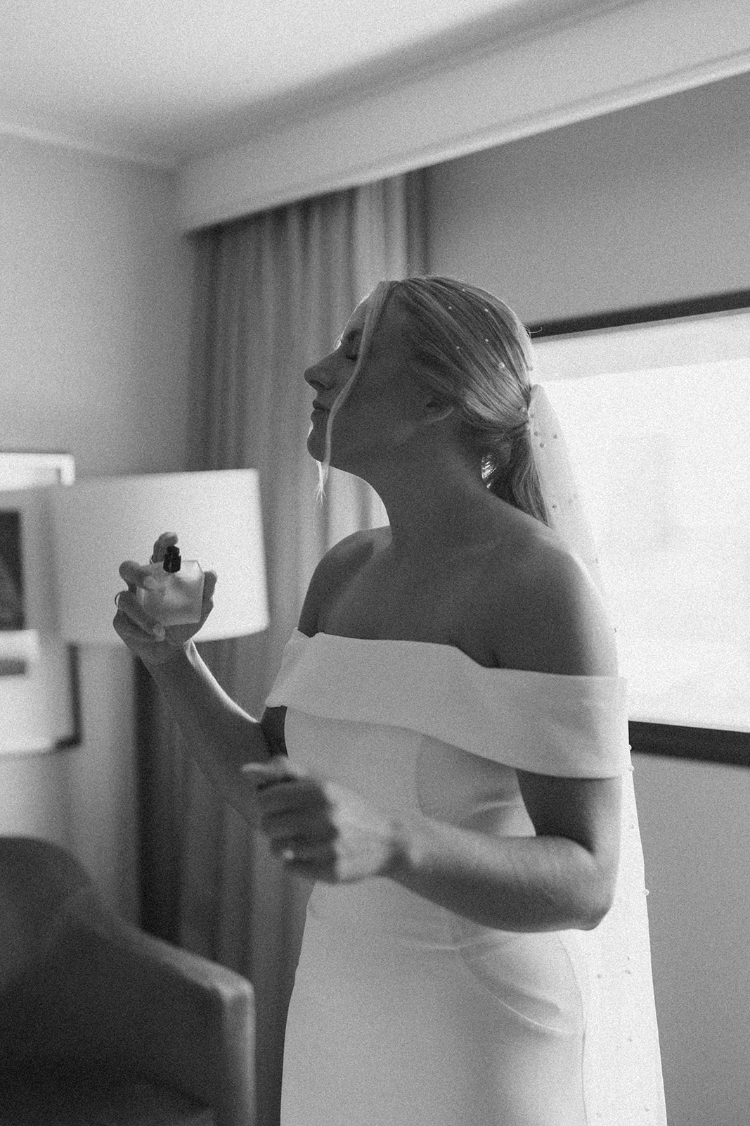 Bride sprays perfume on her chest while she's in her wedding dress before wedding in Wisconsin