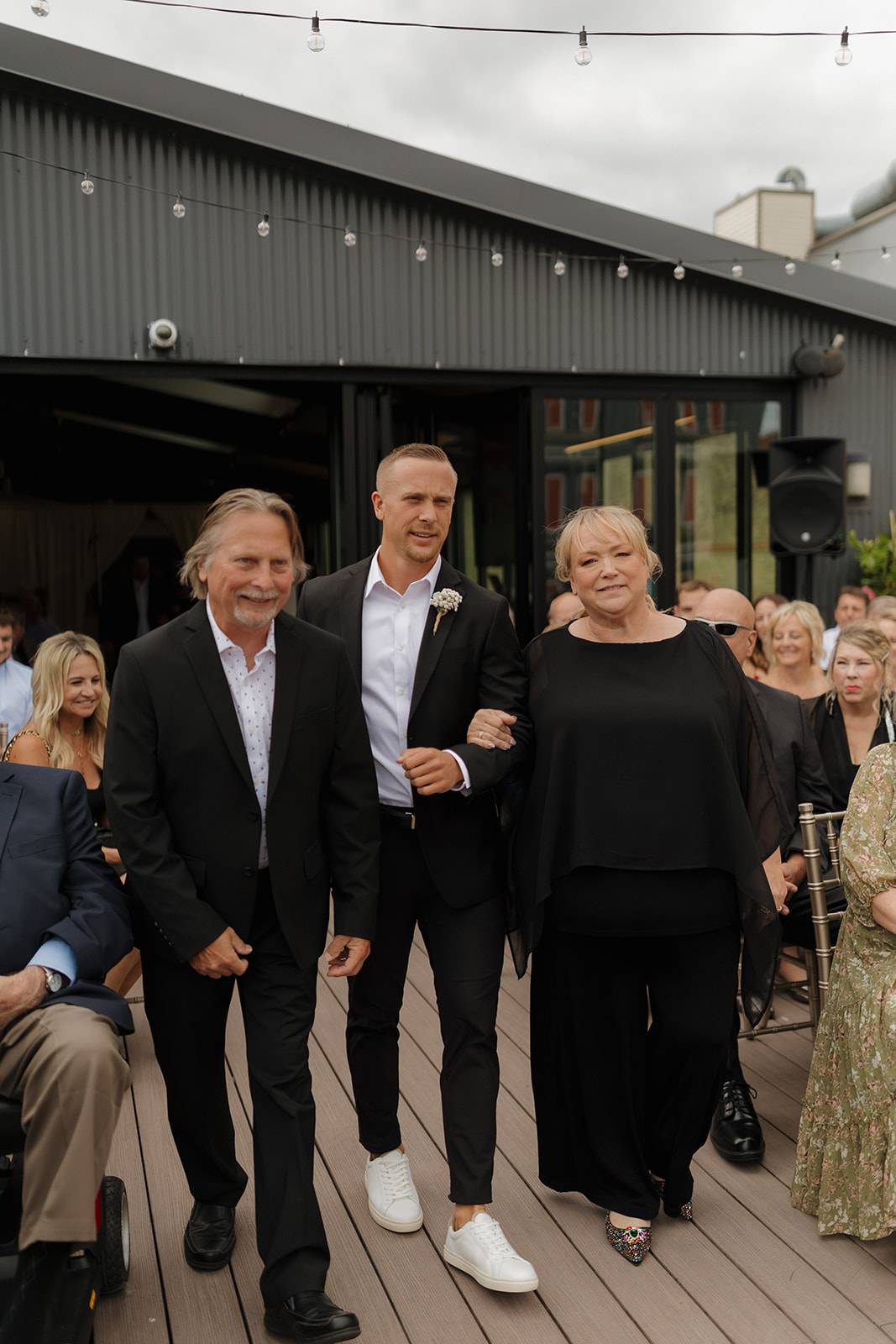 Groom being walked down aisle by parents all wearing black and white clothing.