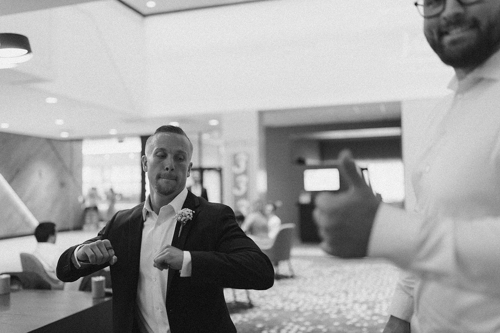 Groom busts out silly dance moves while getting ready with groomsmen in hotel room.
