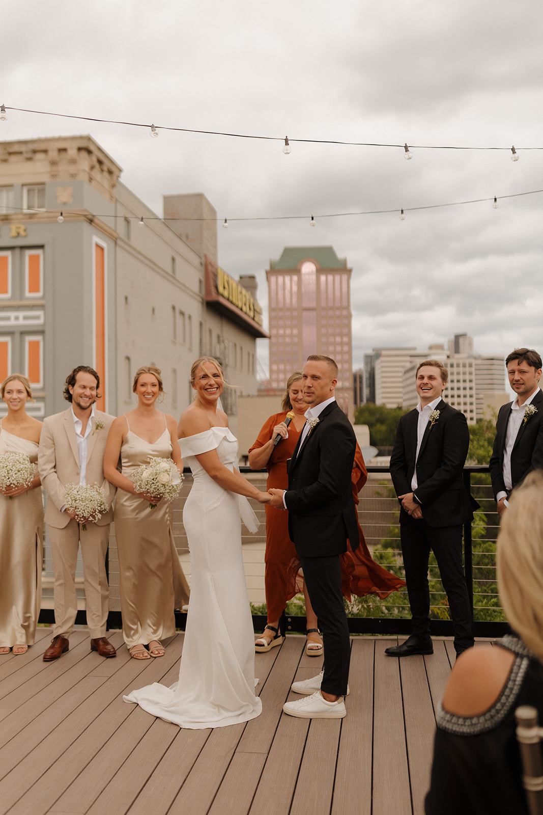 Wedding couple holds hands and laughs together looking at wedding guests