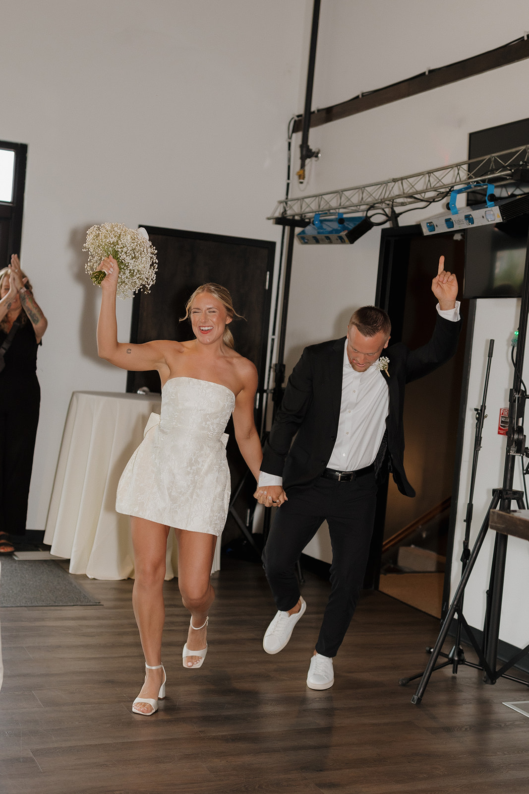Couple joyfully entering their wedding reception, bouquet and hands in the air.