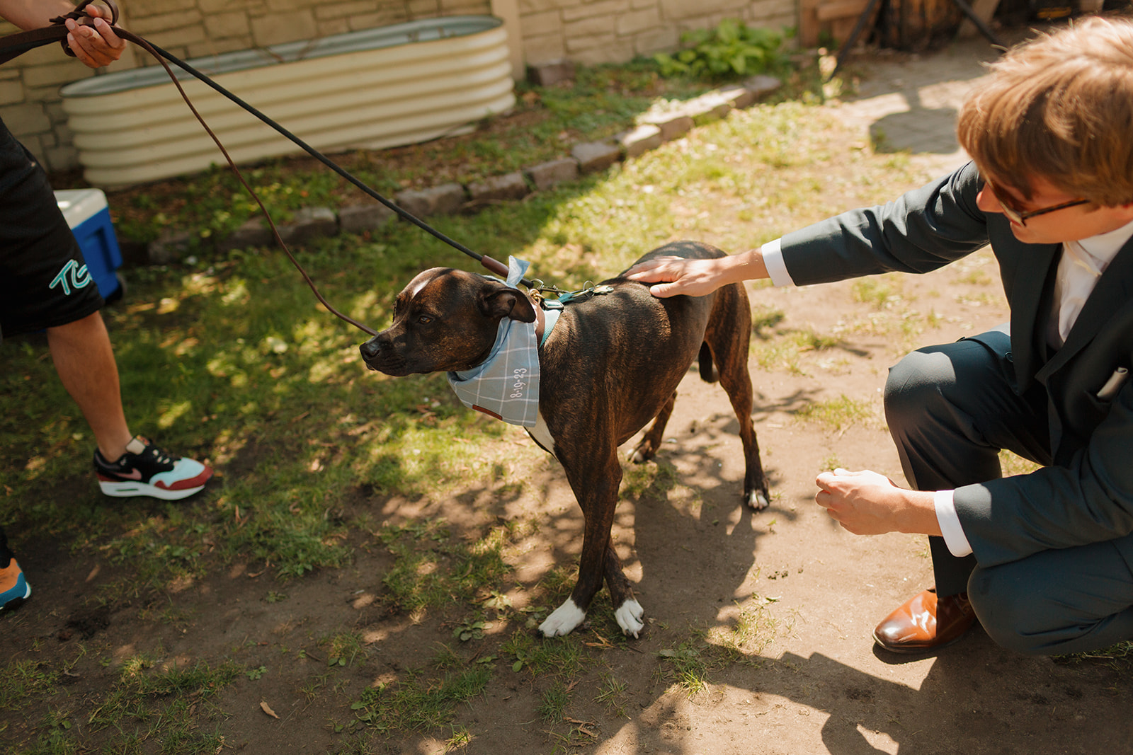 Groom pets dog before wedding at milwaukee wedding venue while dog wears blue bandana