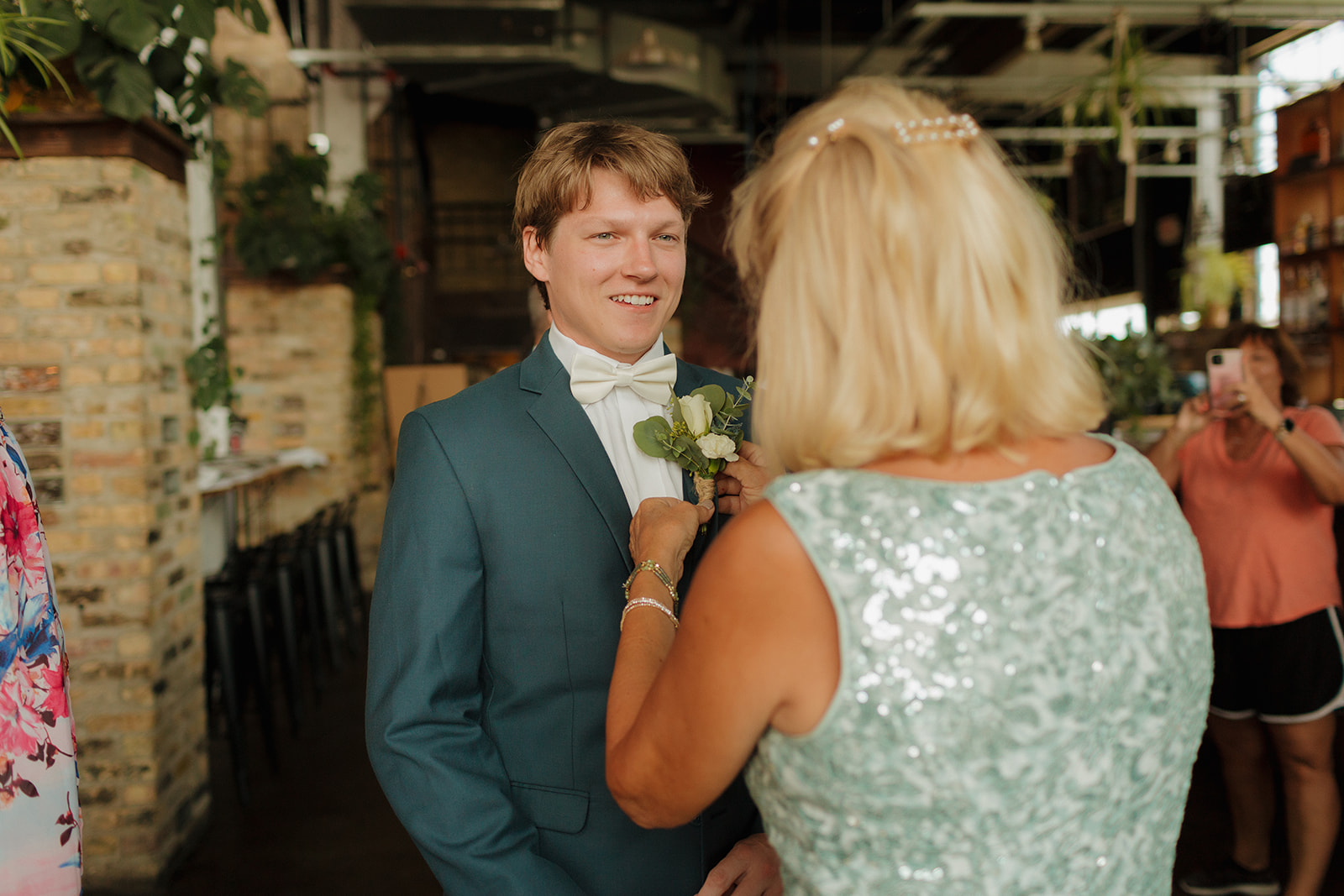 Groom's mother helps adjust boutonniere before wedding at elegant indoor Milwaukee wedding venue