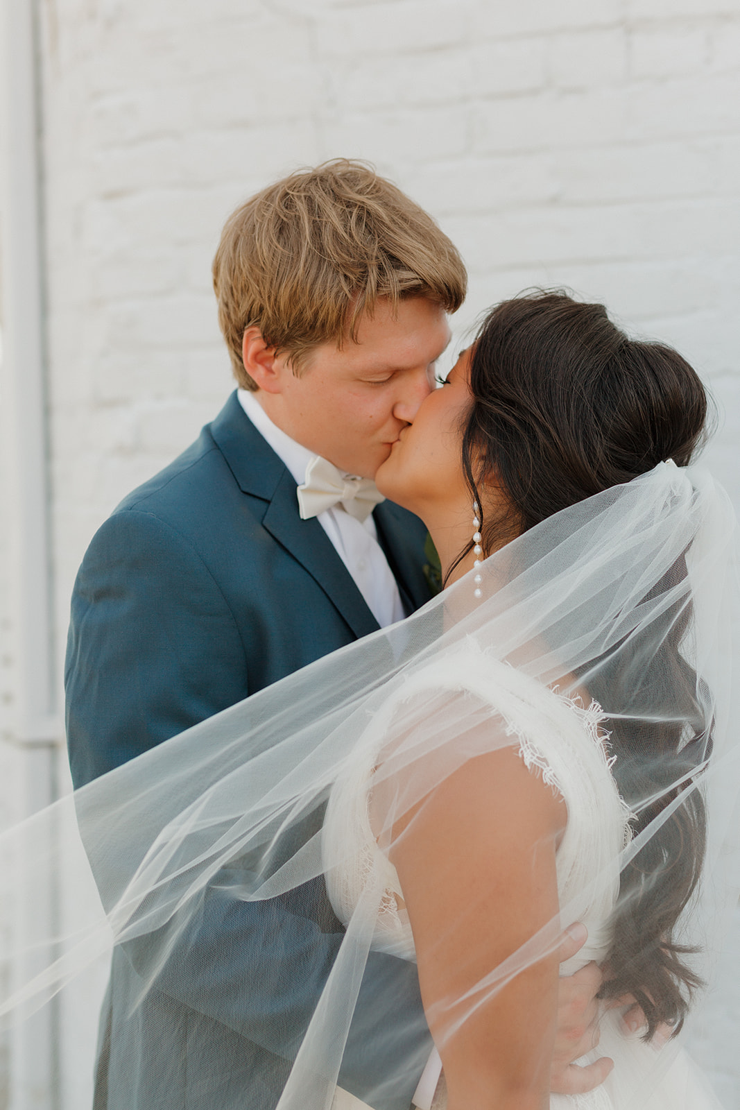 Couple kisses as newly married couple while bride's veil blows in the wind. 