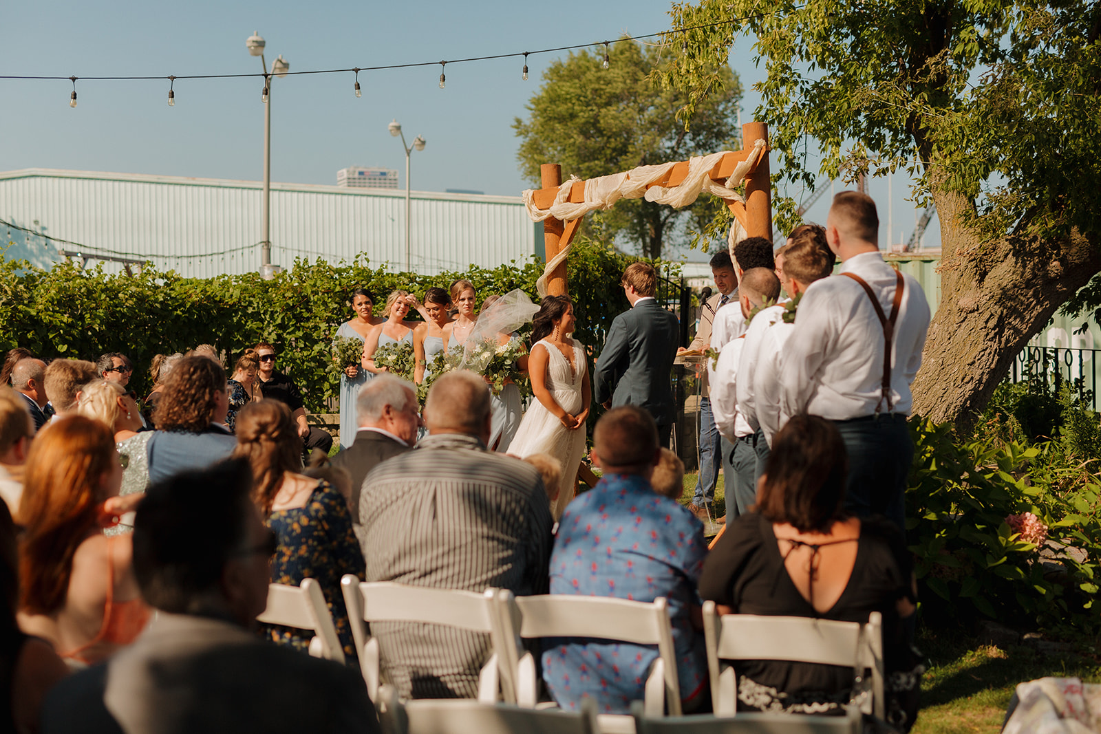 Bride and groom stand at alter together looking at officiant with wedding party and guests supporting them
