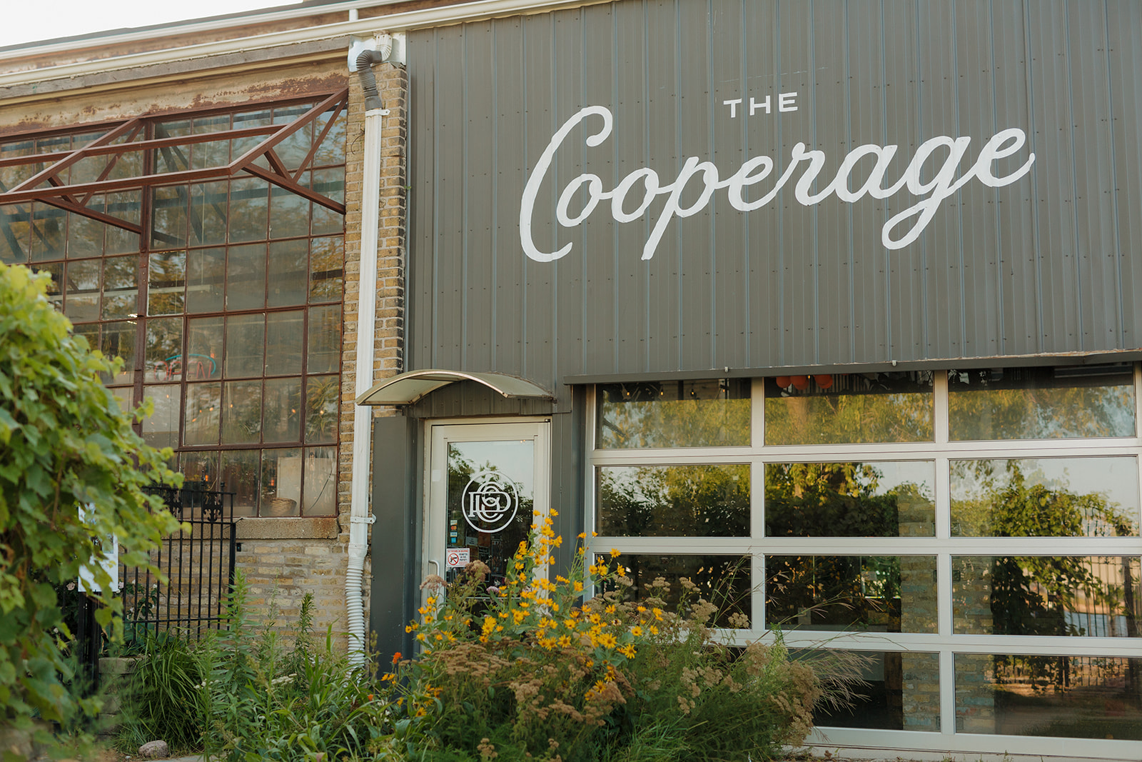 Exterior of The Cooperage, a popular Milwaukee wedding venue, with industrial windows, greenery, and bold signage.
