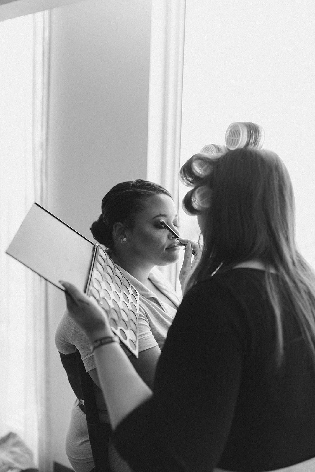 Bride gets makeup done by makeup artist with hair in curlers