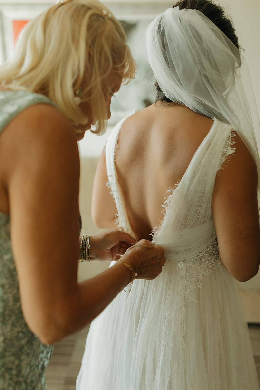 Woman helping bride into wedding dress, buttoning up her wedding gown
