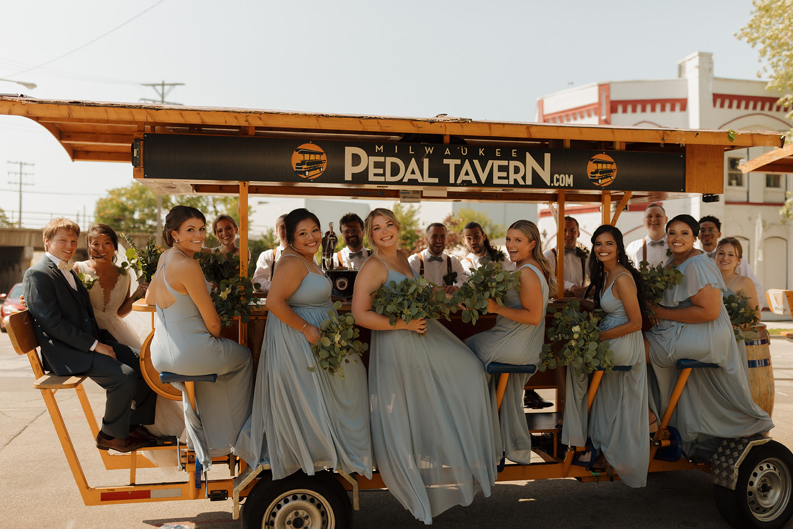 Wedding party sits on a beer cart pedaling through town after wedding at Milwaukee wedding venue