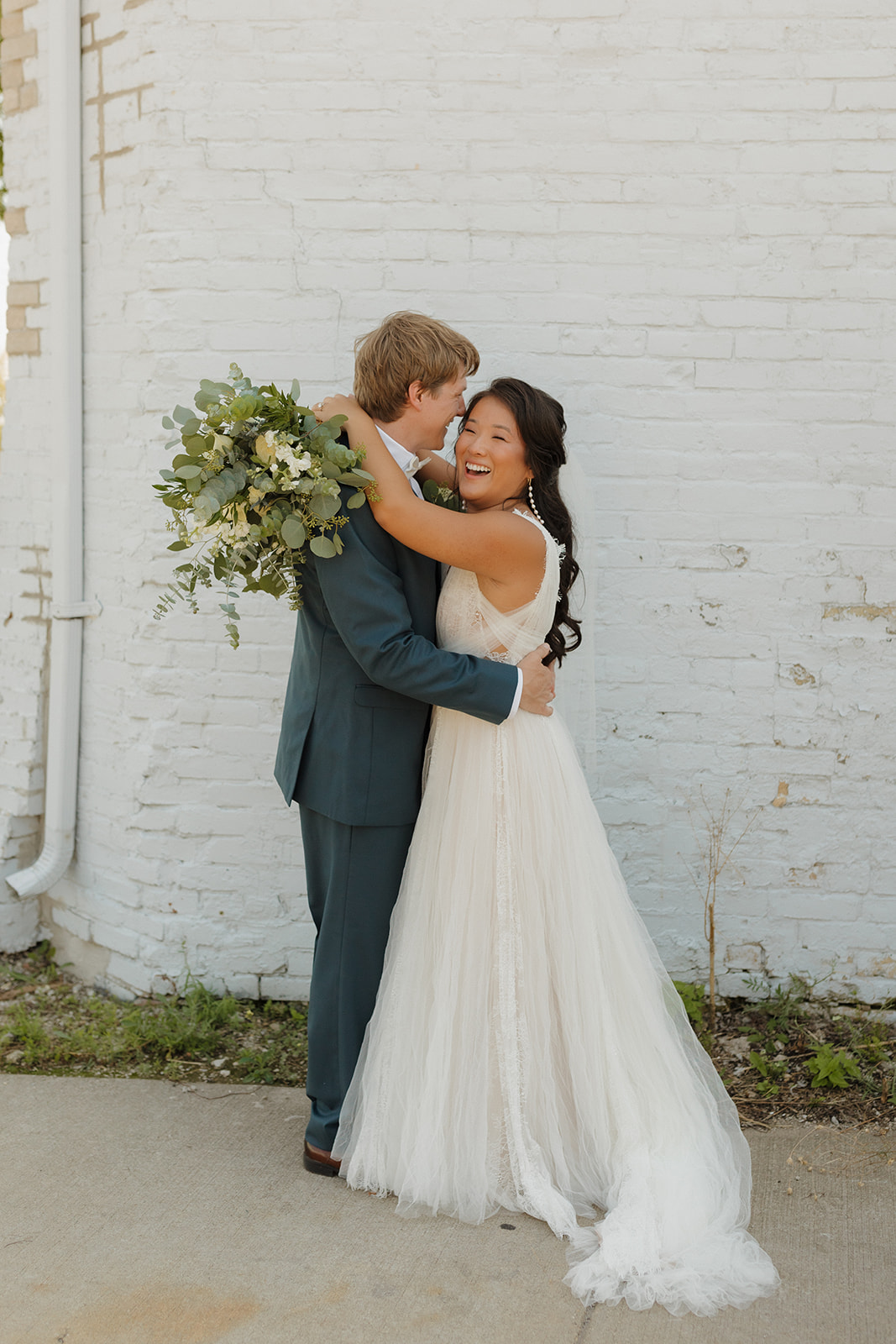 Groom embraces his bride while she laughs casually. 