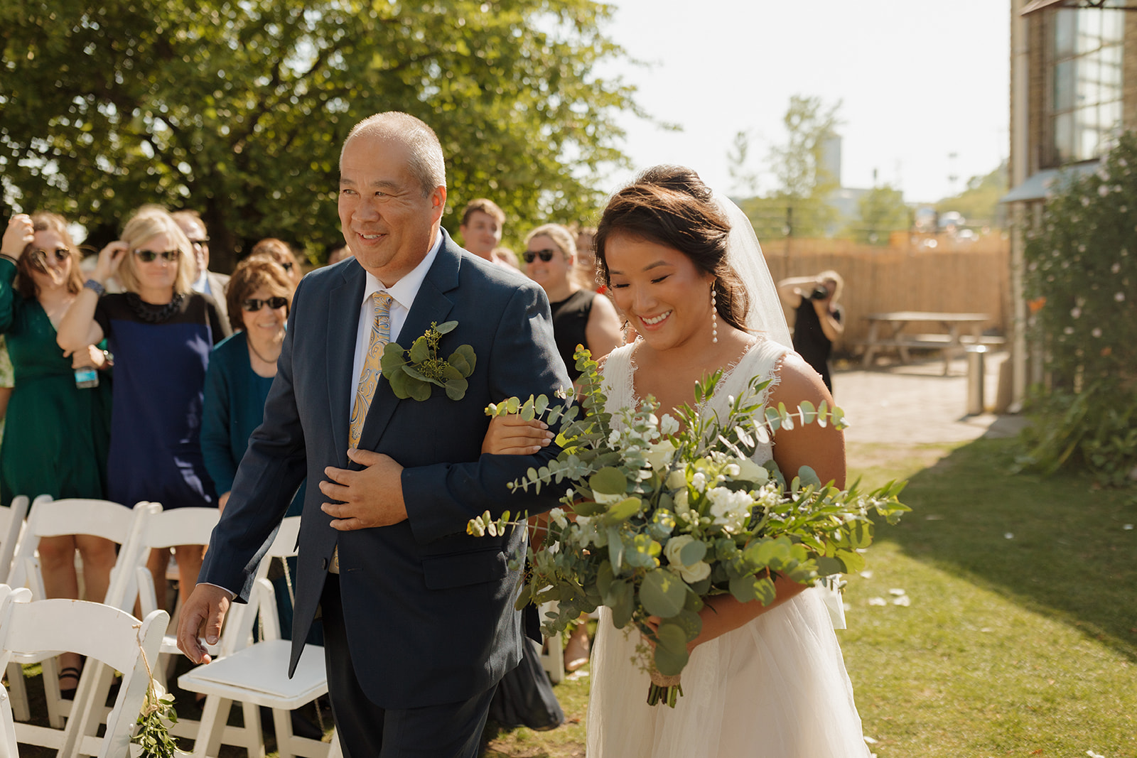 Bride is being escorted down aisle by her father towards her groom