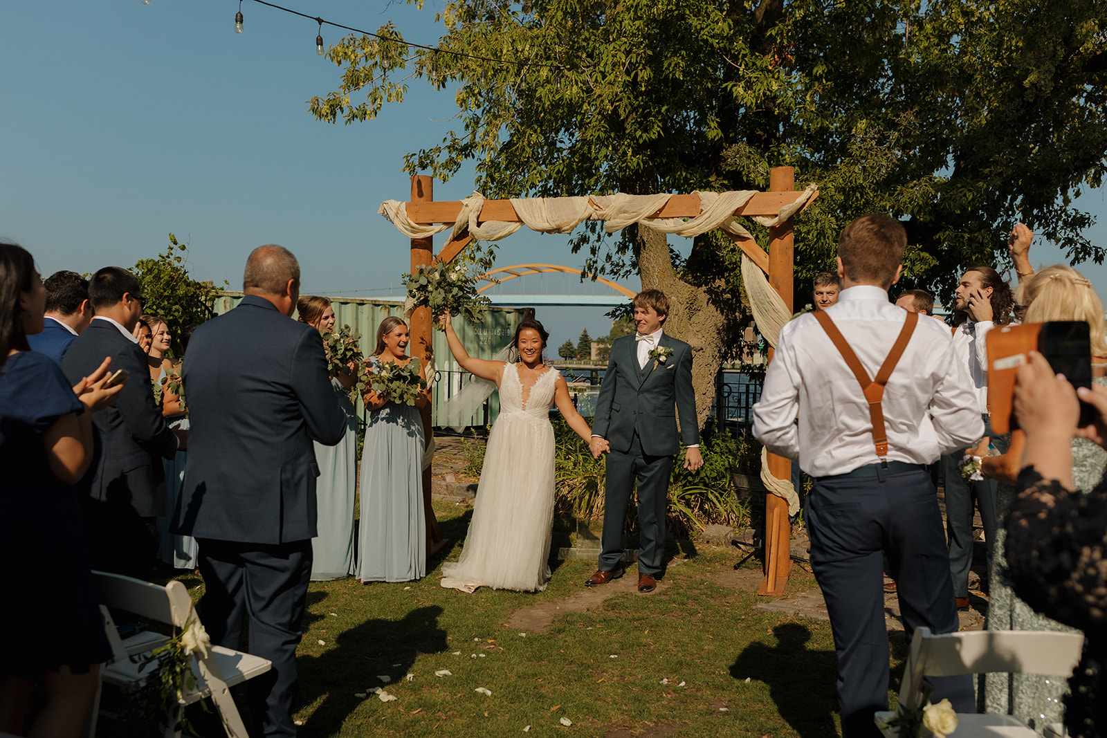 Couple raises hands celebrating recent marriage while bride holds bouquet in the air