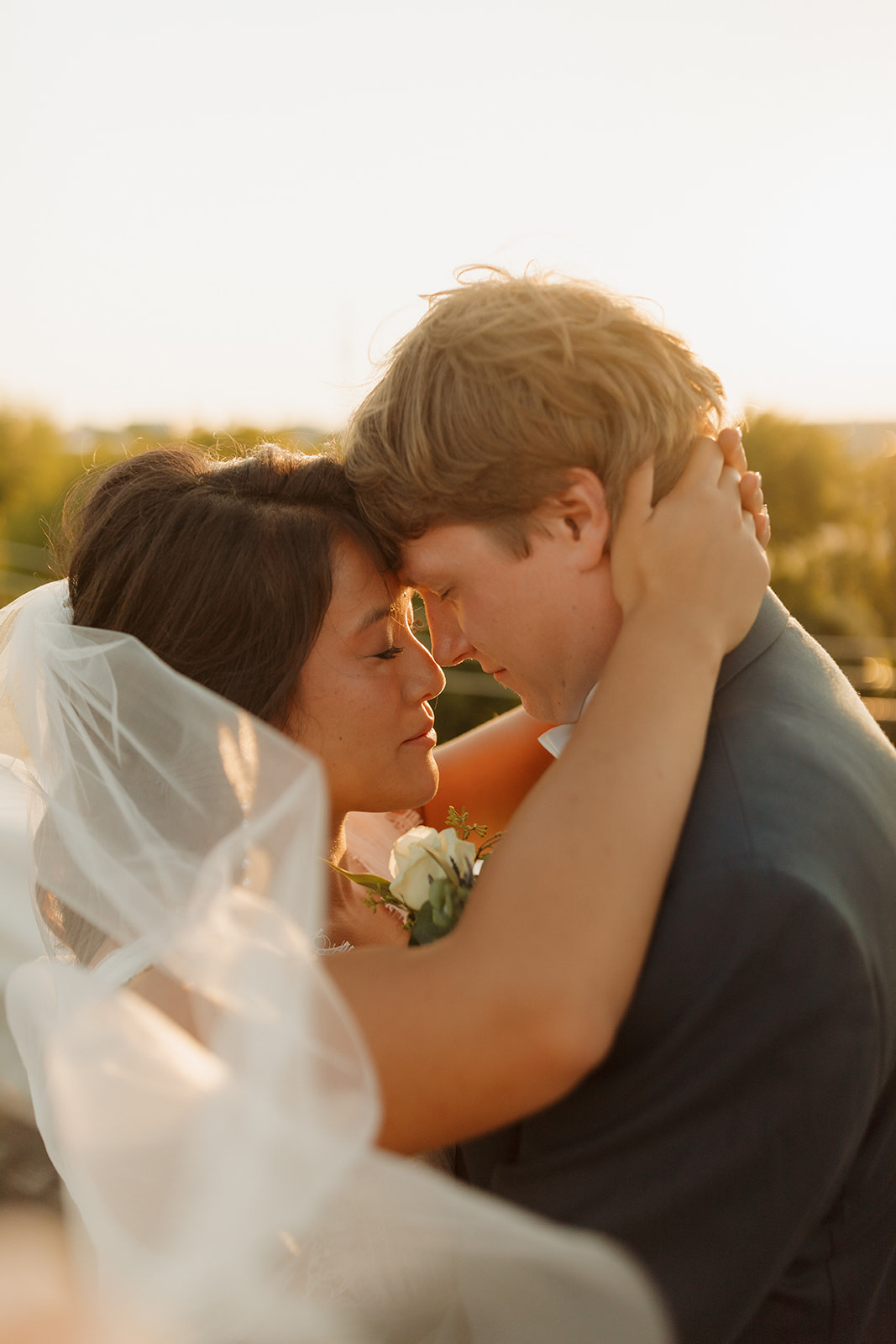 Close-up of an emotional embrace at golden hour as the bride and groom press foreheads, framed by soft light and a flowing veil.