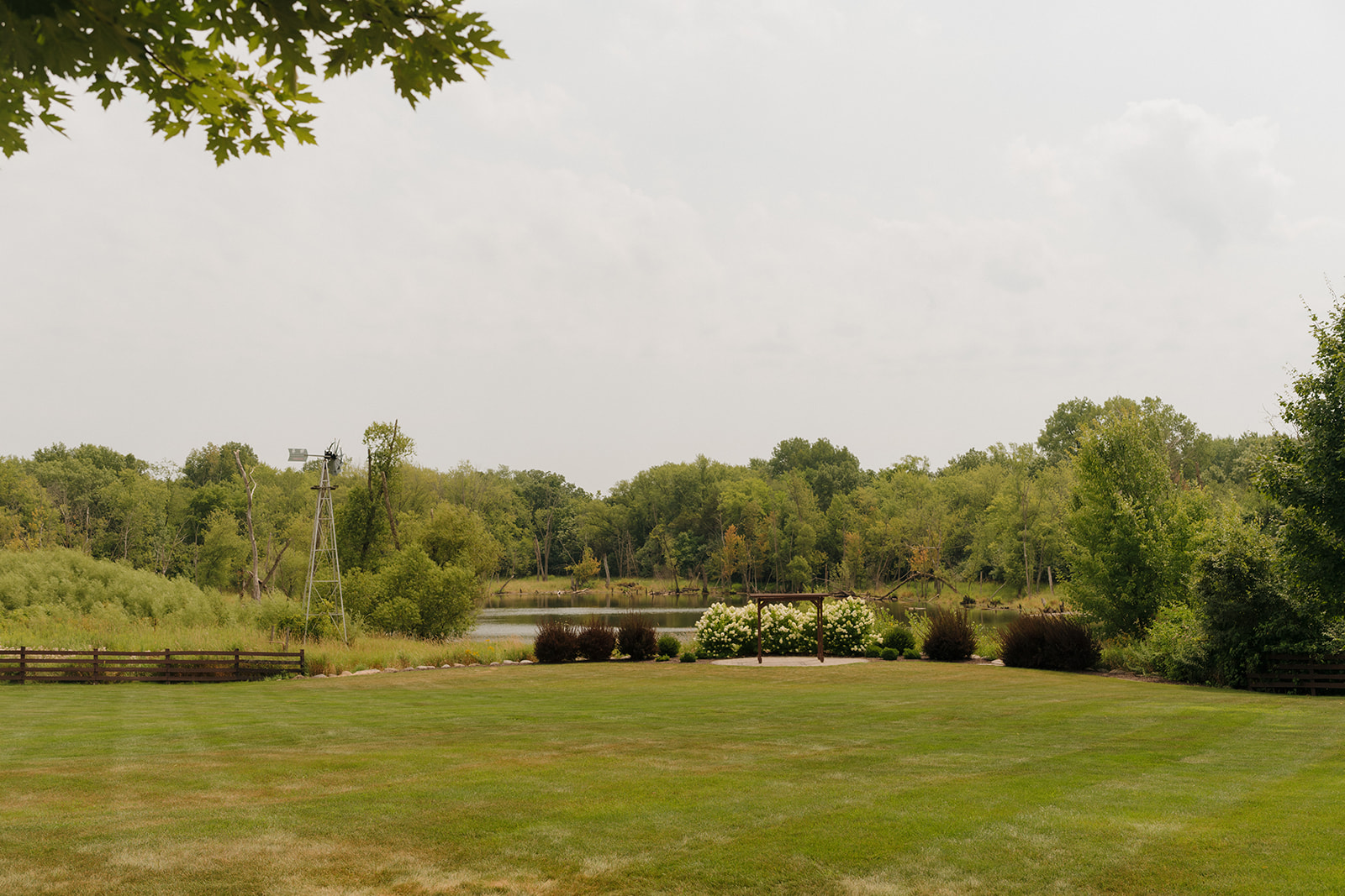 View of an outdoor ceremony site with a wooden arbor, pond, and open lawn at a peaceful Wisconsin wedding venue.