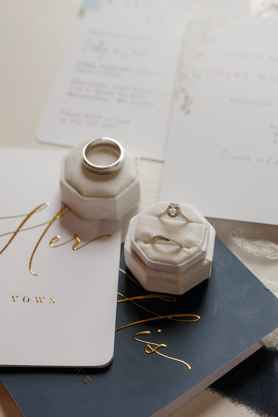 Flat lay of wedding details including rings, vow books, and invitations with gold accents.