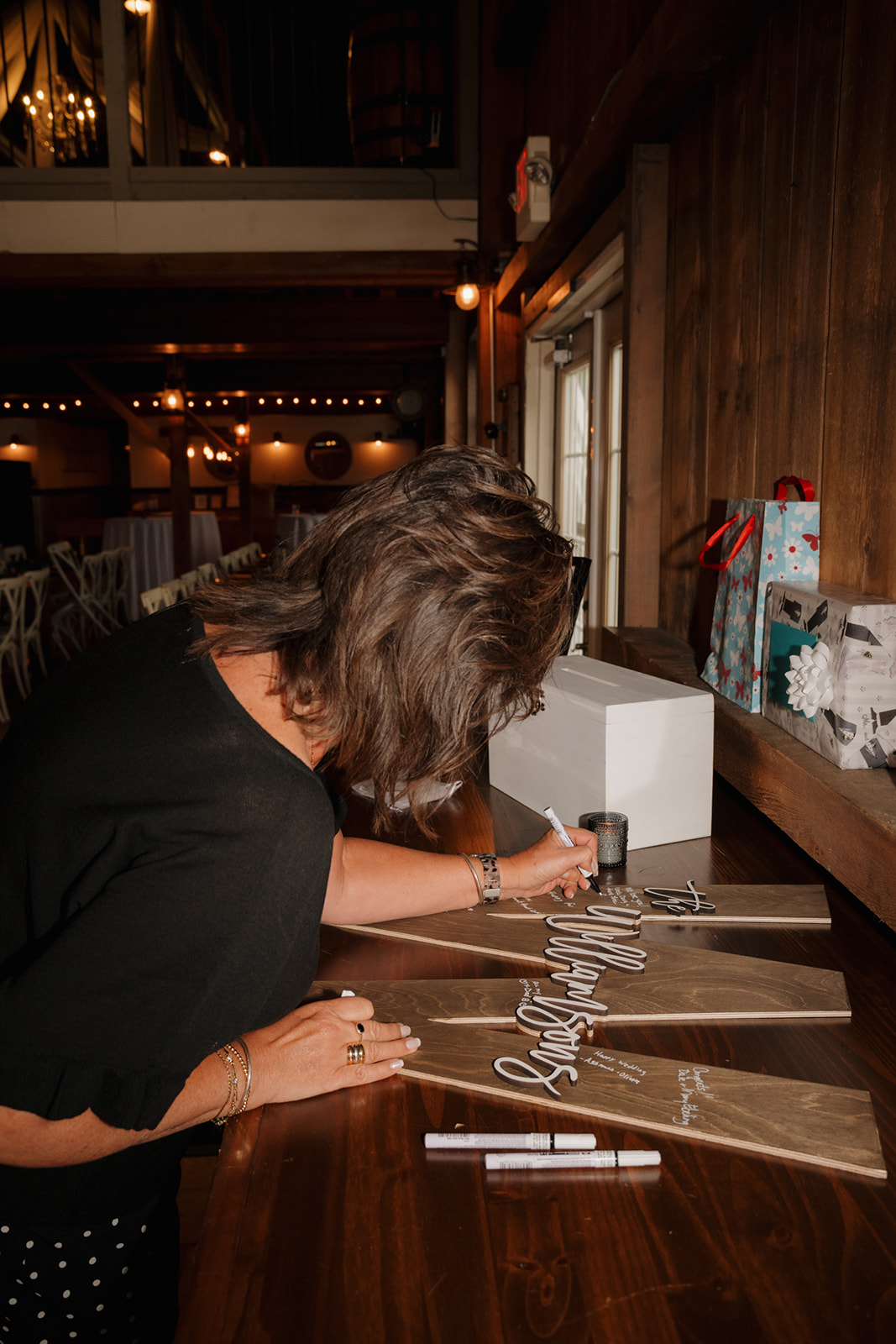 Guest signing a wooden paddle guestbook in a cozy barn reception space.