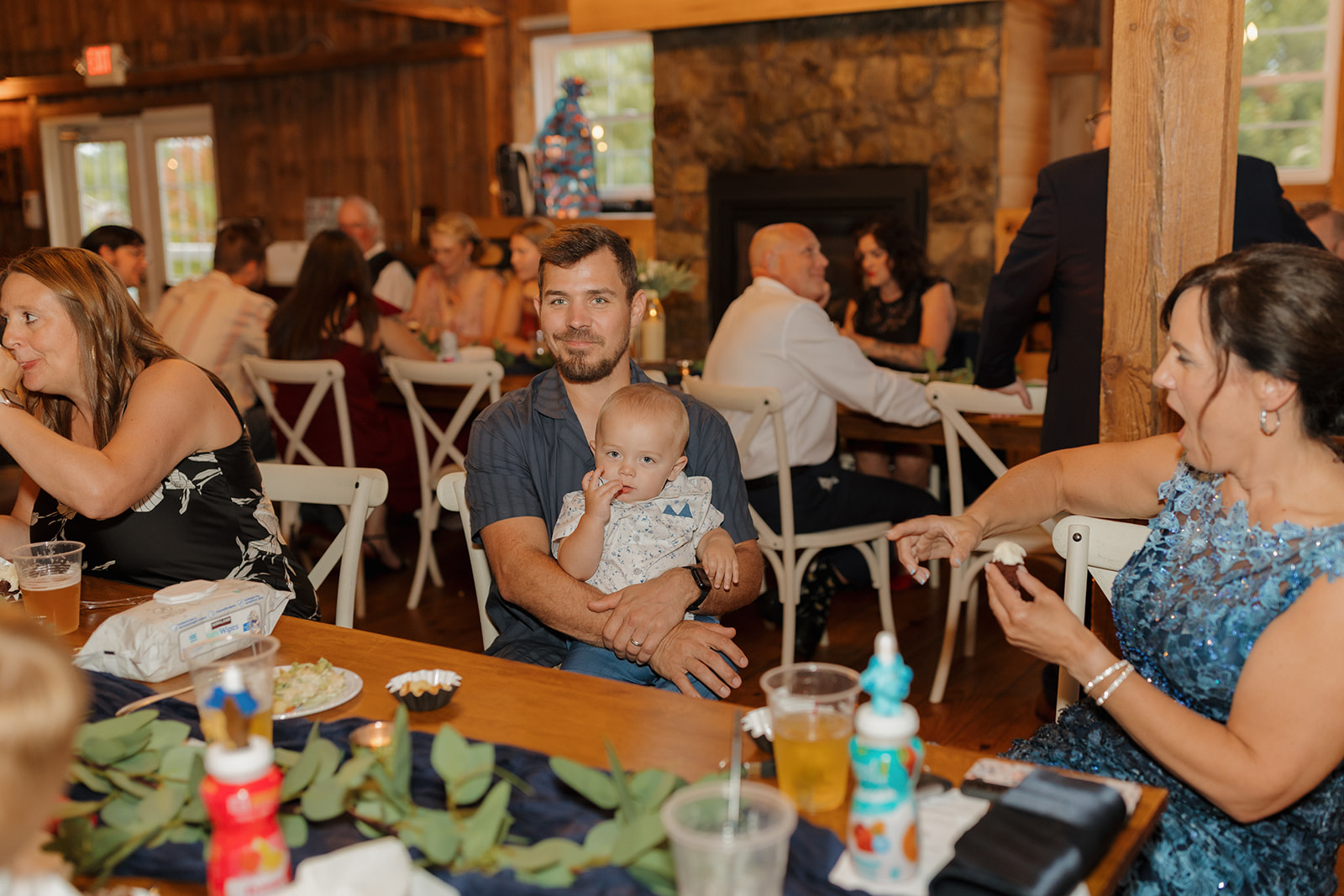 Reception guests laughing and chatting at long wooden tables during the wedding dinner.