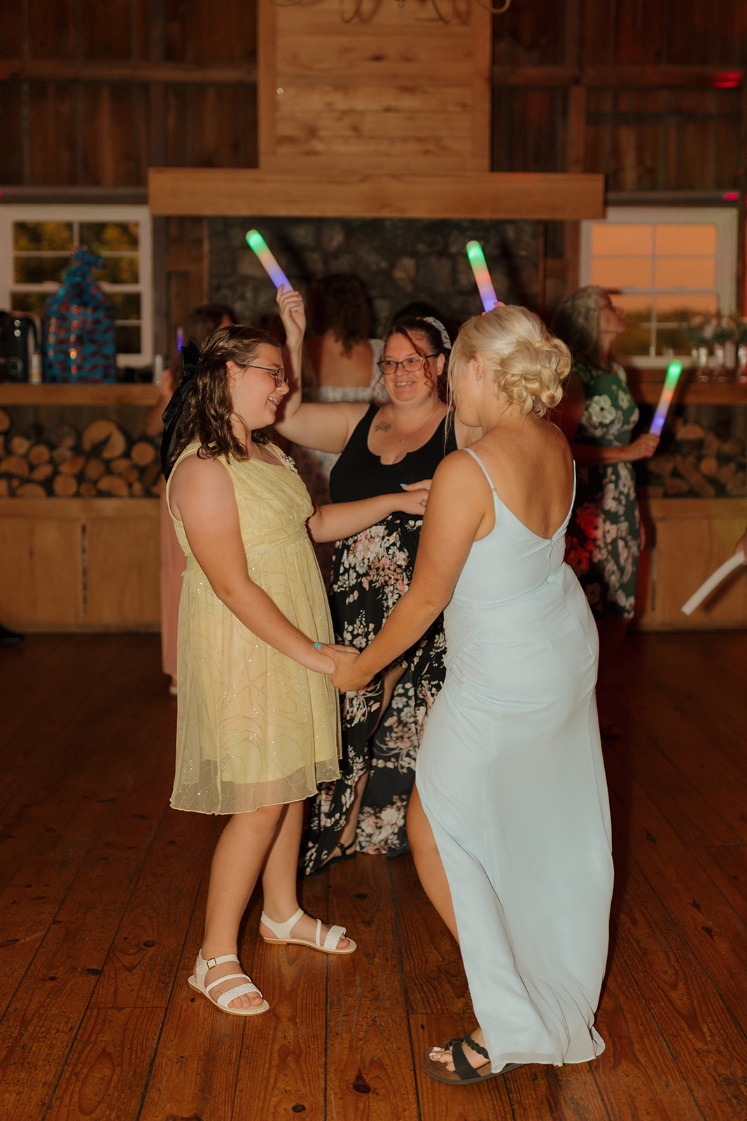 Guests dancing with glow sticks on the wooden floor of a rustic Wisconsin wedding venue.