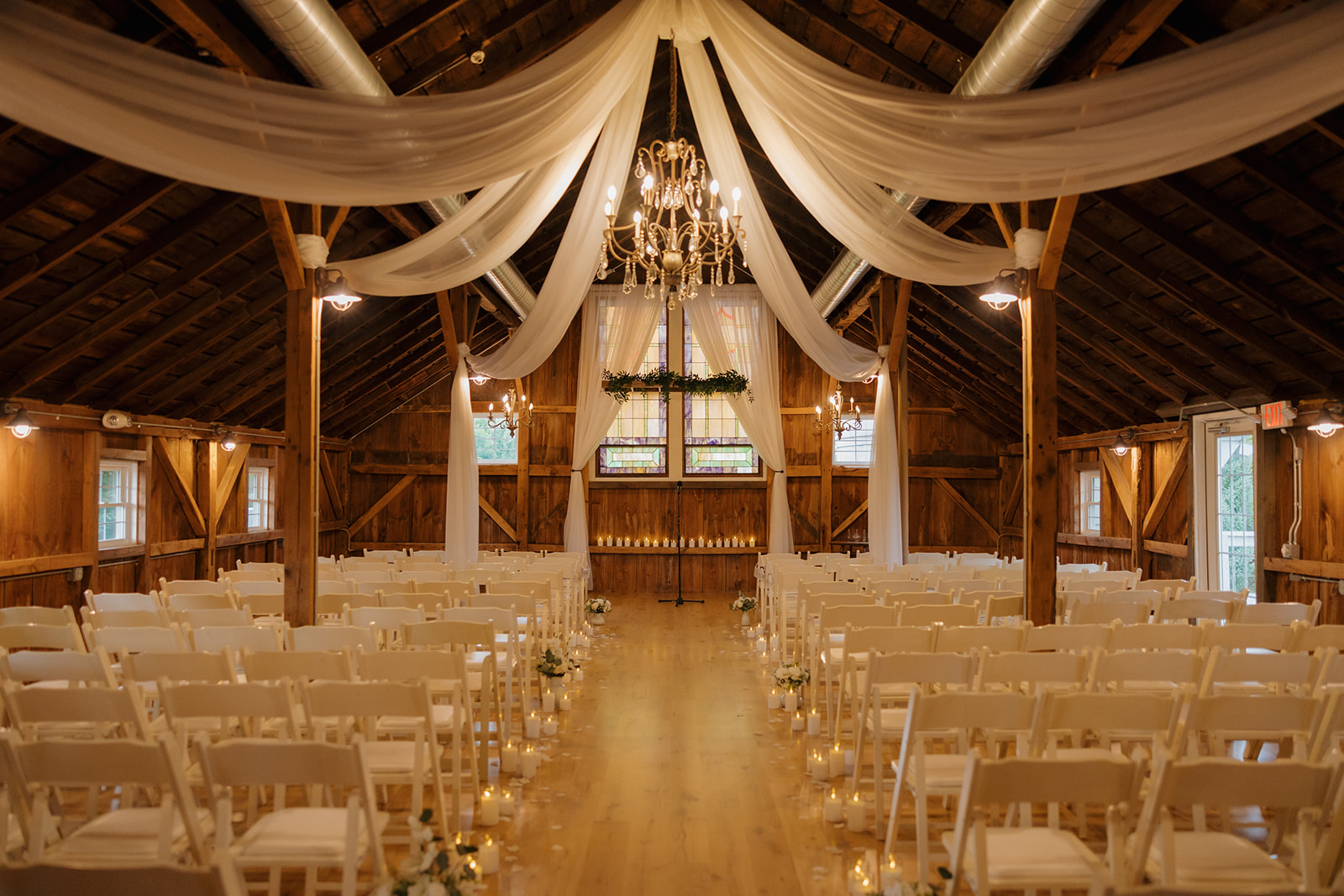 Elegant barn ceremony setup with draped fabric, soft candlelight, and chandeliers at a rustic Wisconsin wedding venue.