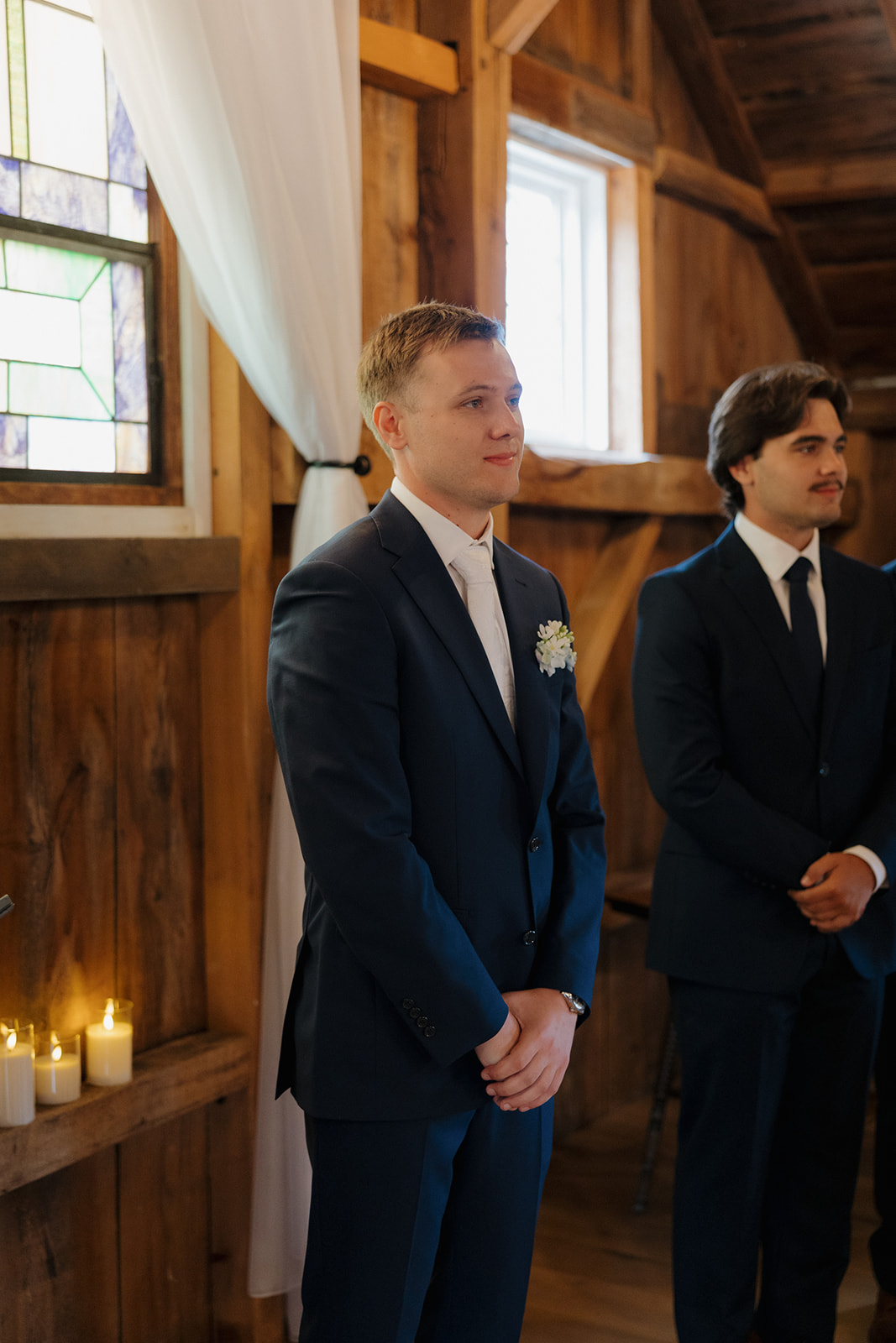 Groom standing at the altar, waiting for the ceremony to begin, with soft window light behind him.
