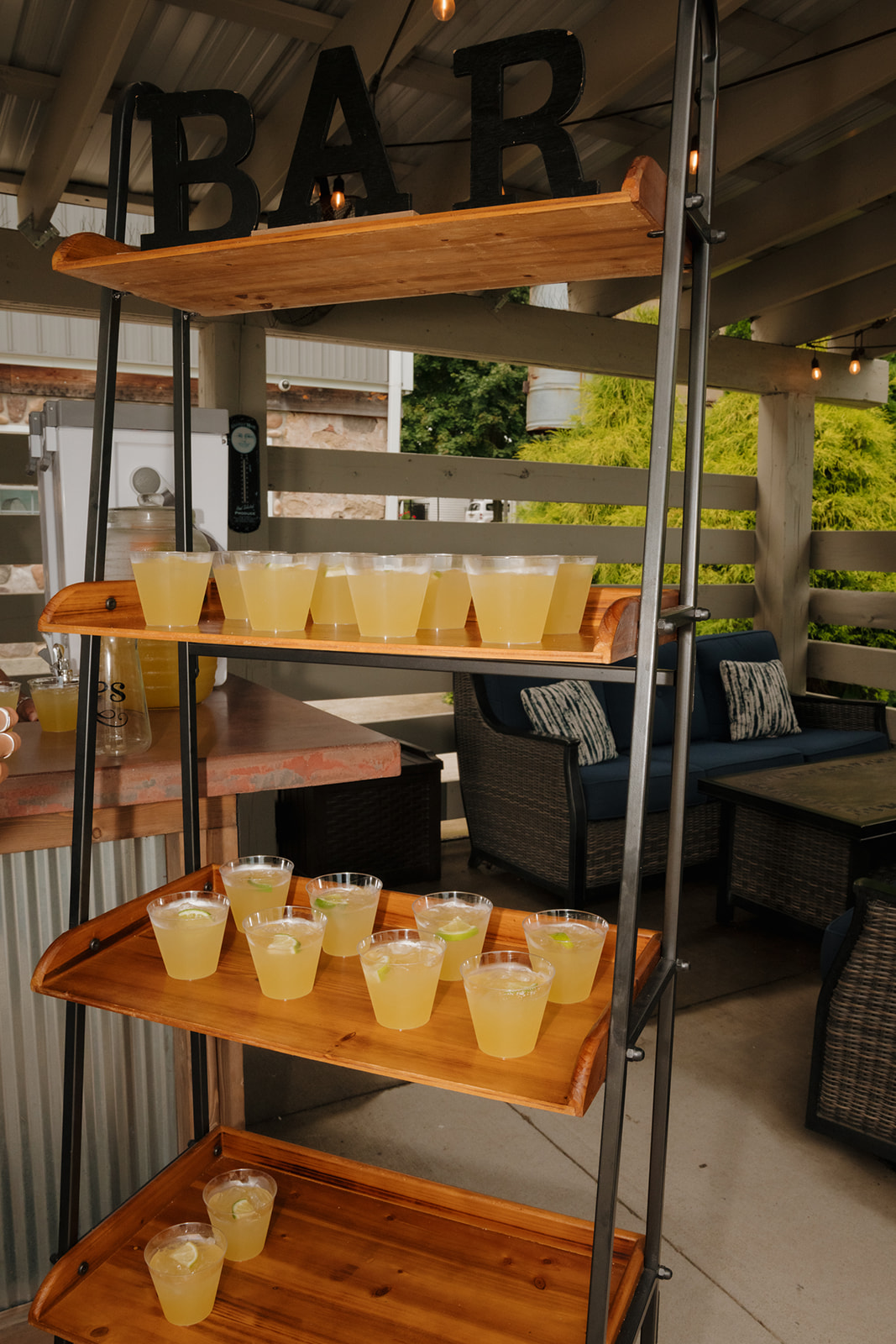 Bar setup with wooden shelves holding rows of pre-poured margaritas under a covered outdoor space.
