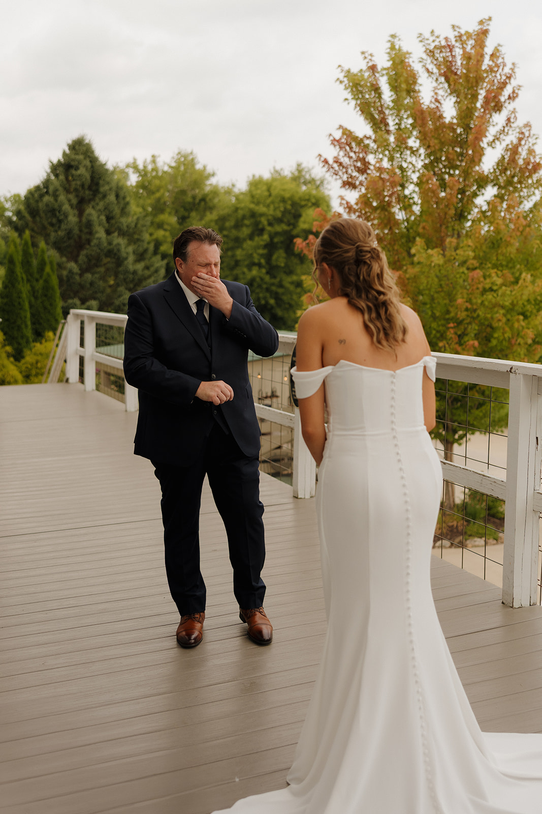 Father of bride covers mouth and gets emotional seeing his daughter for the first time in her wedding dress. 