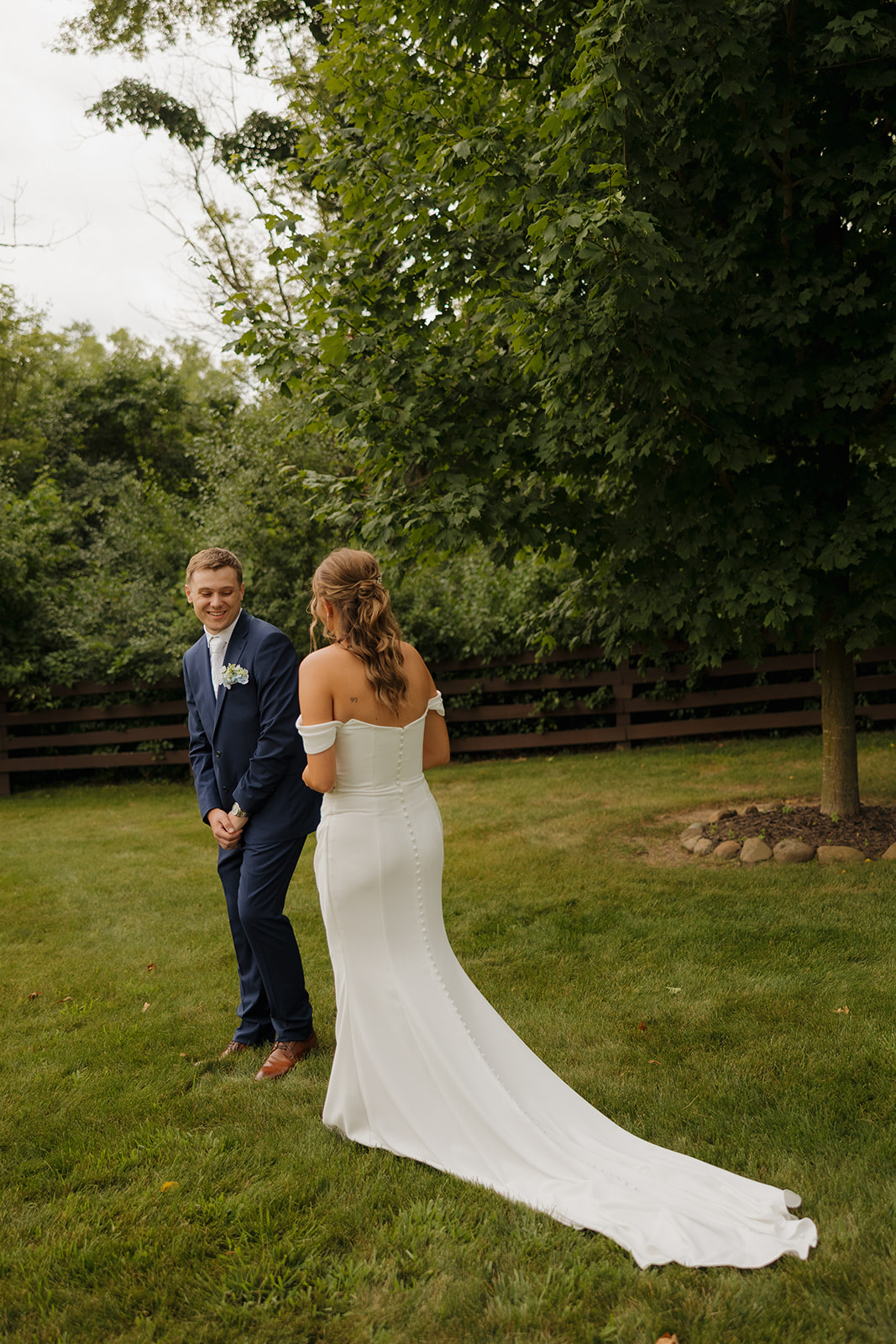 Groom smiling as bride approaches during their first look surrounded by greenery.