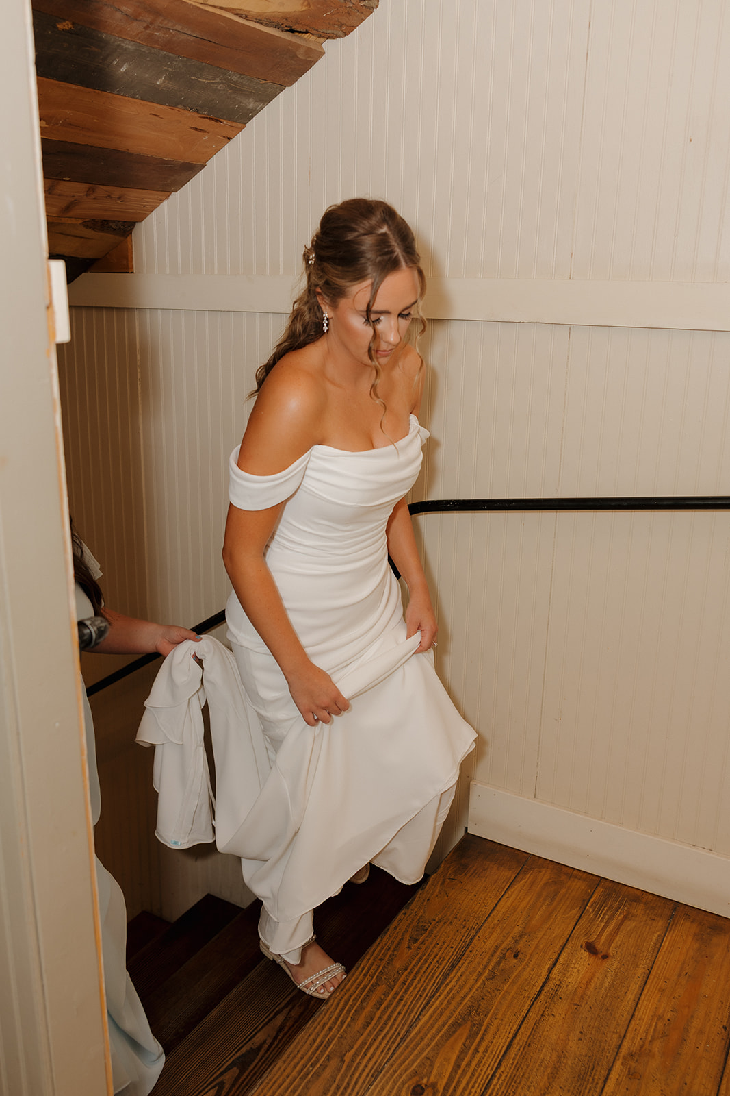Bride walking up rustic wood stairs, holding her dress and smiling before the ceremony.
