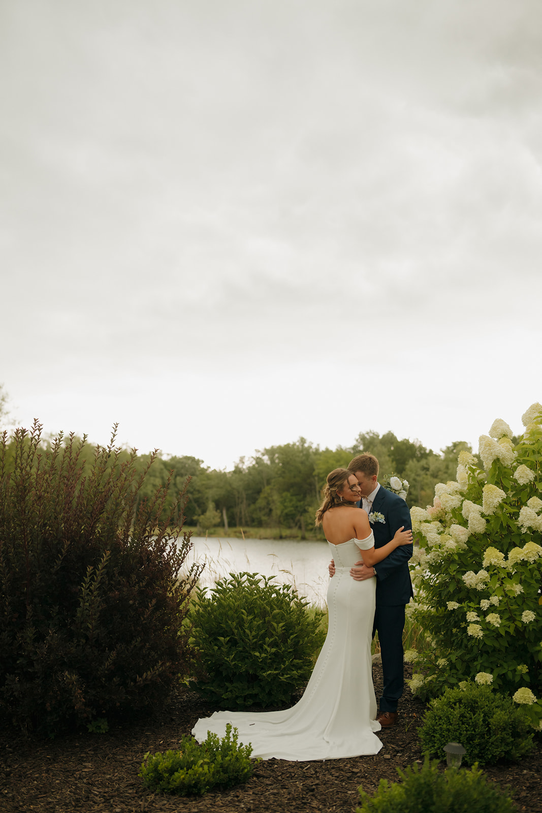 Bride and groom embracing by a peaceful lakeside garden at a Wisconsin wedding venue.