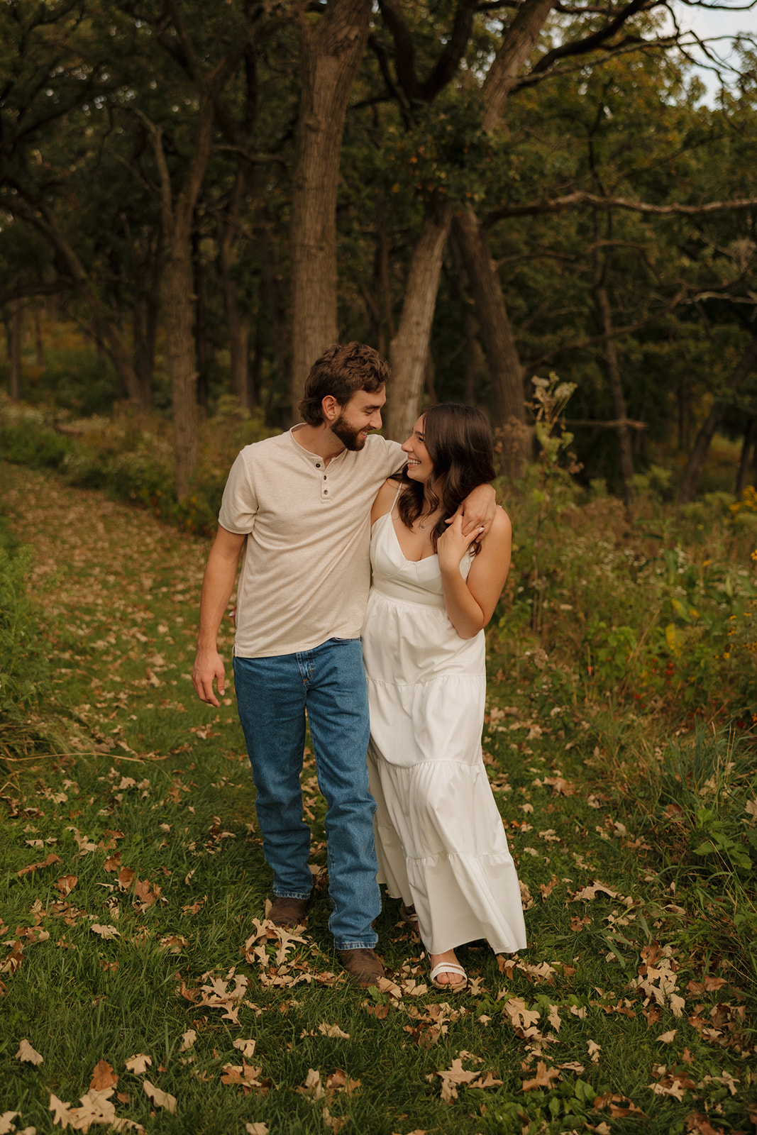 Couple walking closely together through a forest trail in Madison WI, smiling and wrapped up in each other.