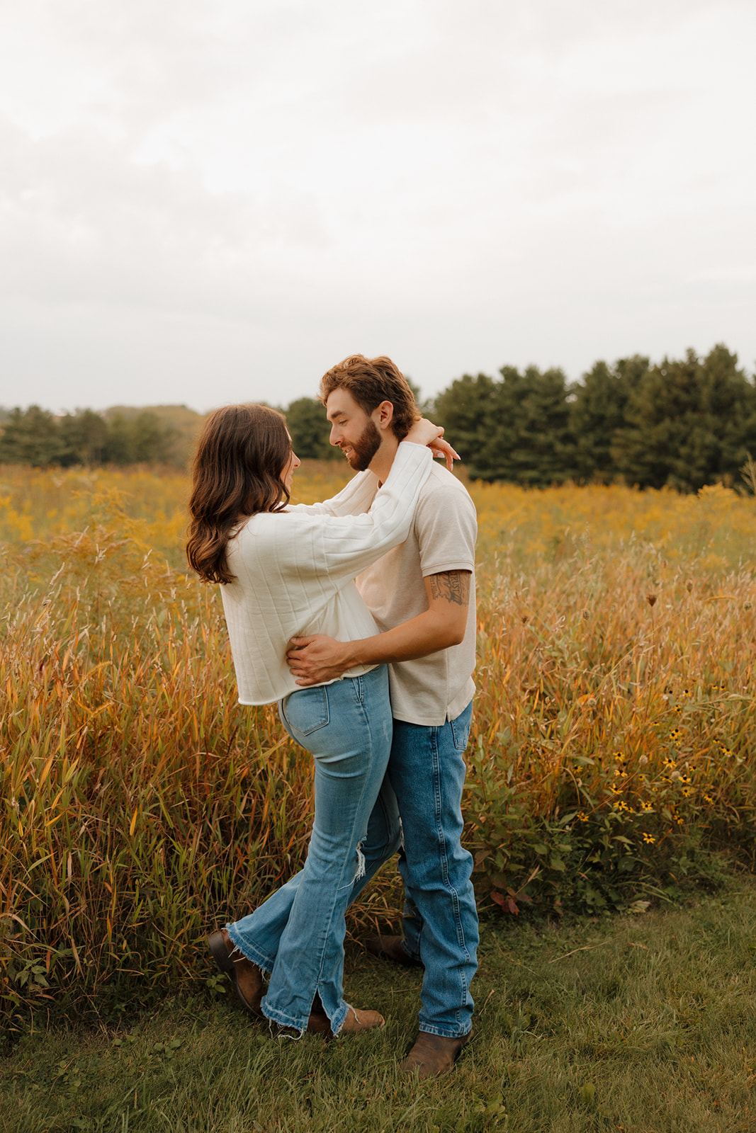 Engagement photo of a couple wrapped in an embrace, standing in a dreamy Madison WI field with soft fall colors.