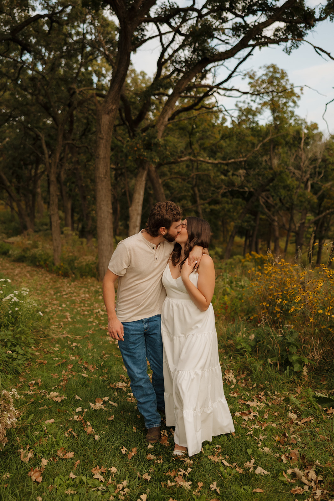 Sweet kiss shared by a couple walking through a wooded trail in Madison WI, with wildflowers lining the path.