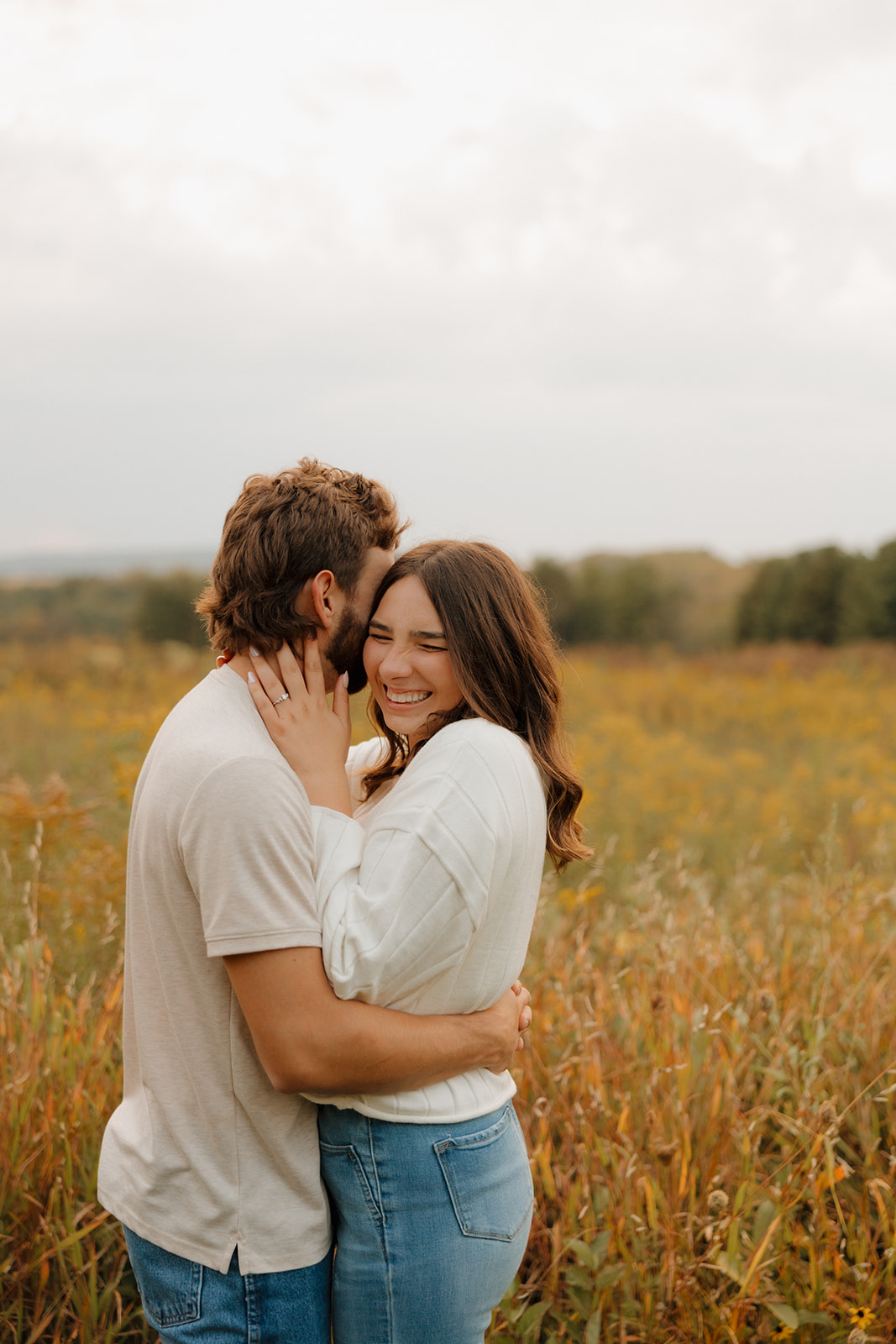 Woman laughing as her partner whispers to her during a fall session in a Madison WI wildflower field.