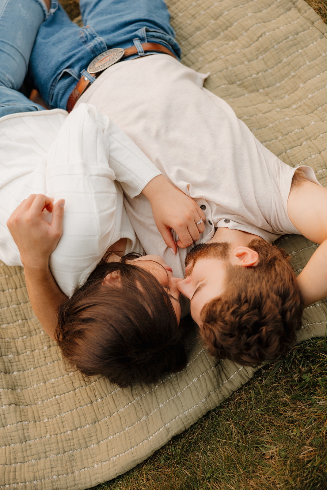 Intimate moment of a couple laying on a blanket in a grassy Madison WI field, forehead to forehead.