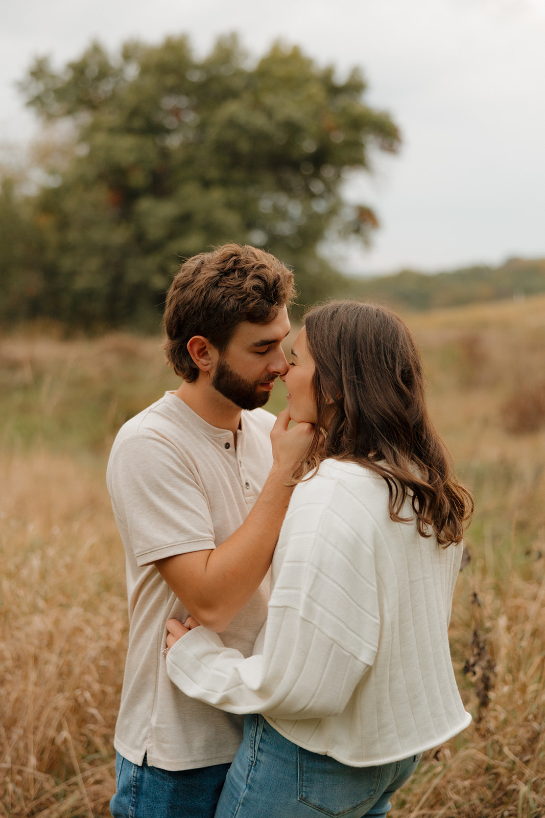 Candid moment of a couple holding each other in a grassy Madison WI field, leaning in for a kiss.