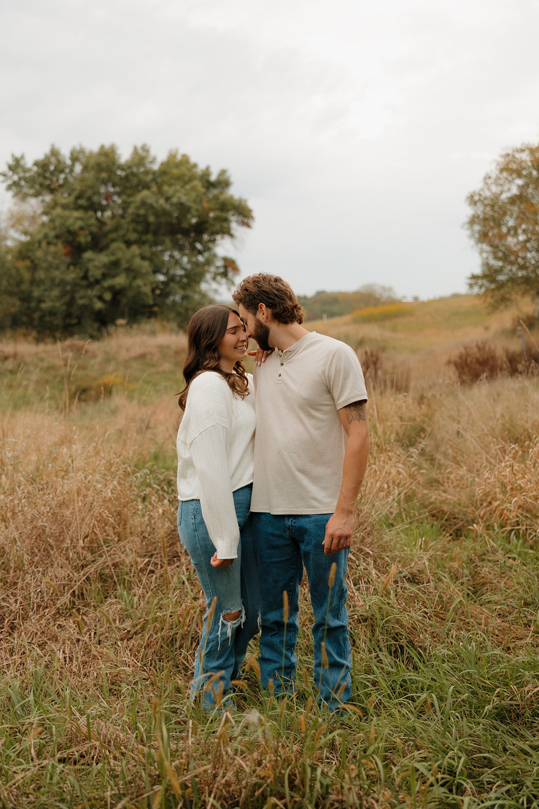 Playful, candid moment of a couple standing in a Madison WI field, leaning in close with matching grins.