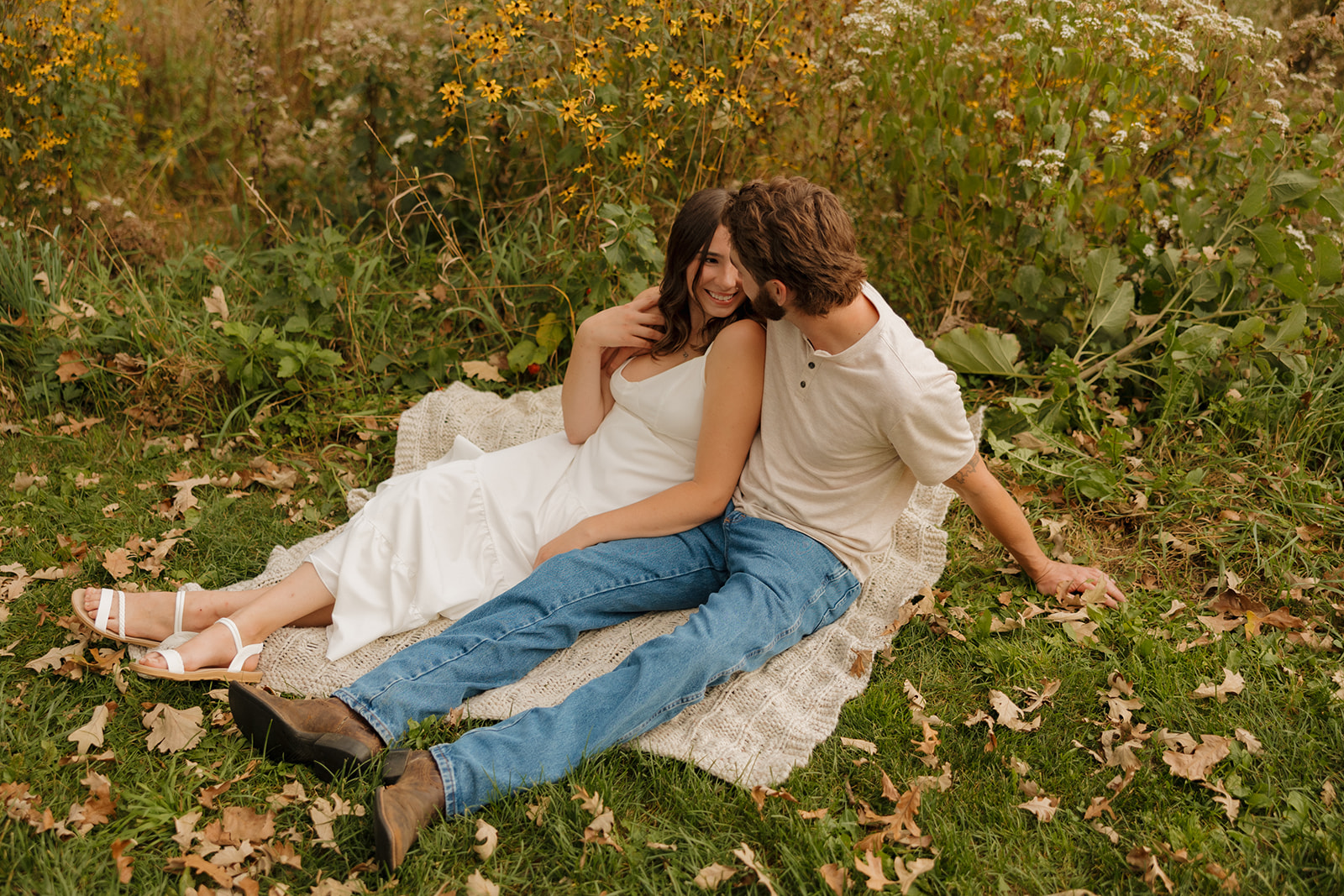 Couple sitting on a cozy blanket in a field of wildflowers near Madison WI, sharing a quiet, joyful moment.